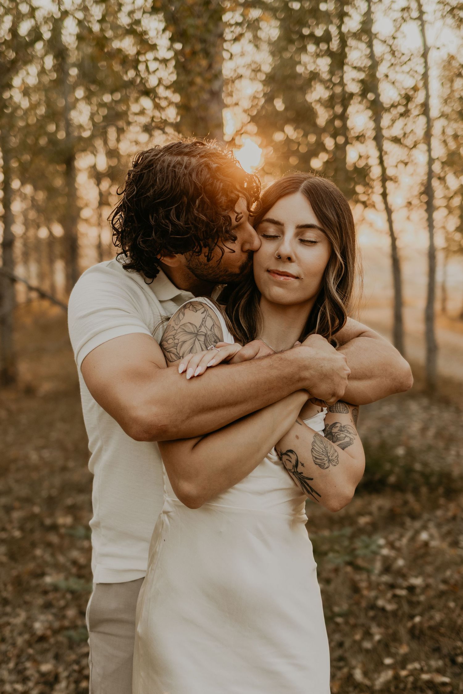 A romantic couple embraces in a sunlit forest during golden hour.