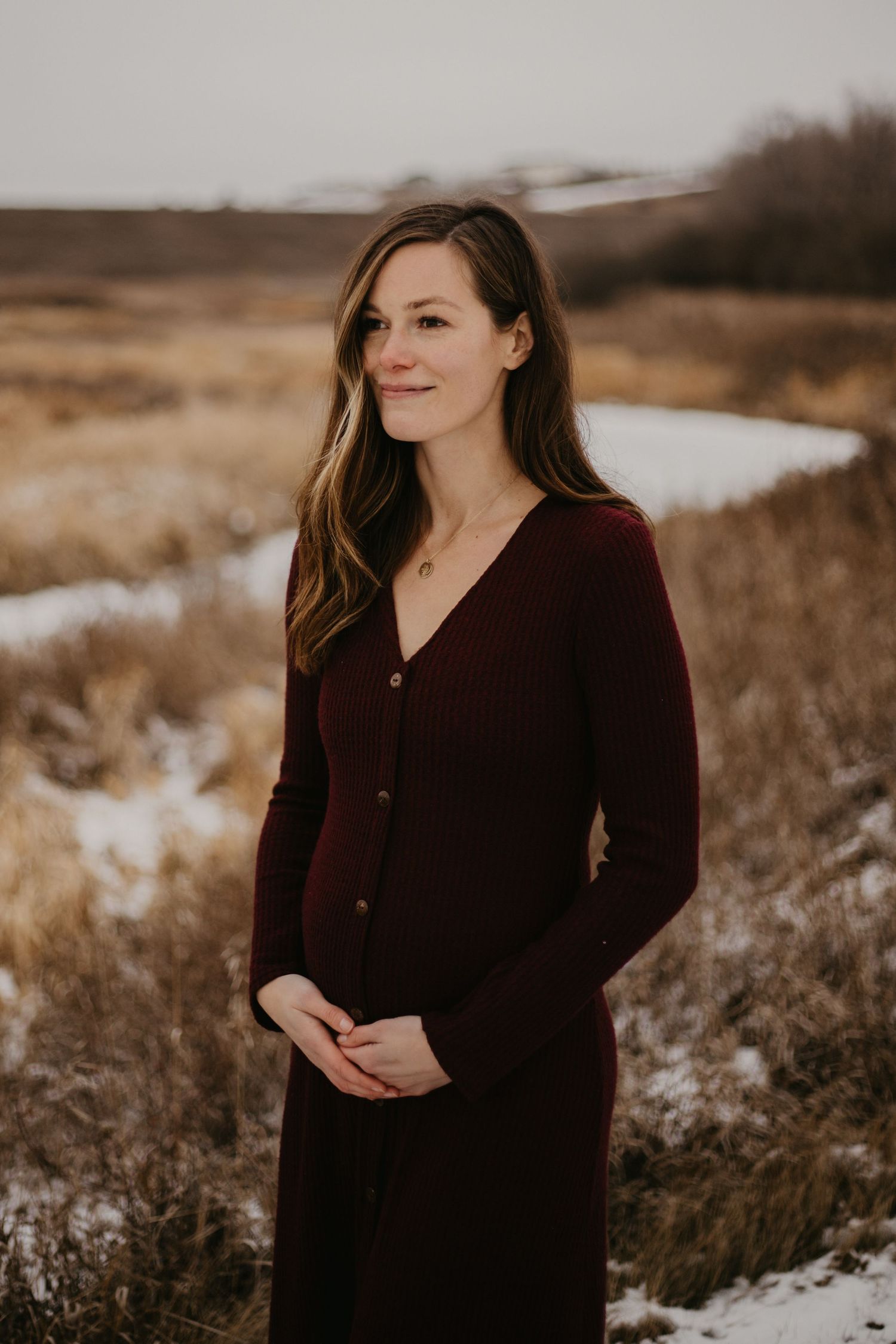 A person in a burgundy sweater dress stands in a snowy winter field.