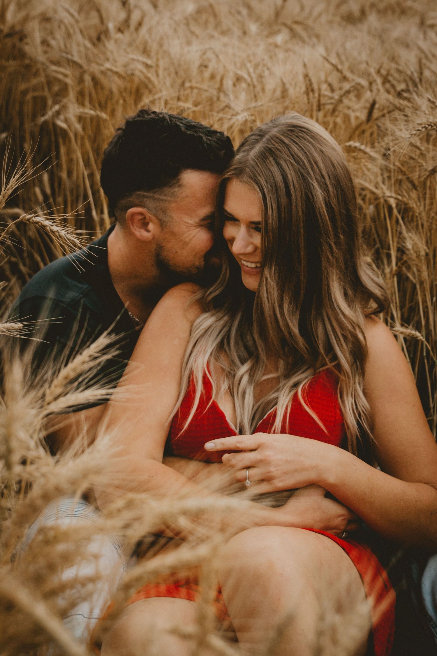 Intimate moment between couple among swaying wheat stalks during golden hour photoshoot.