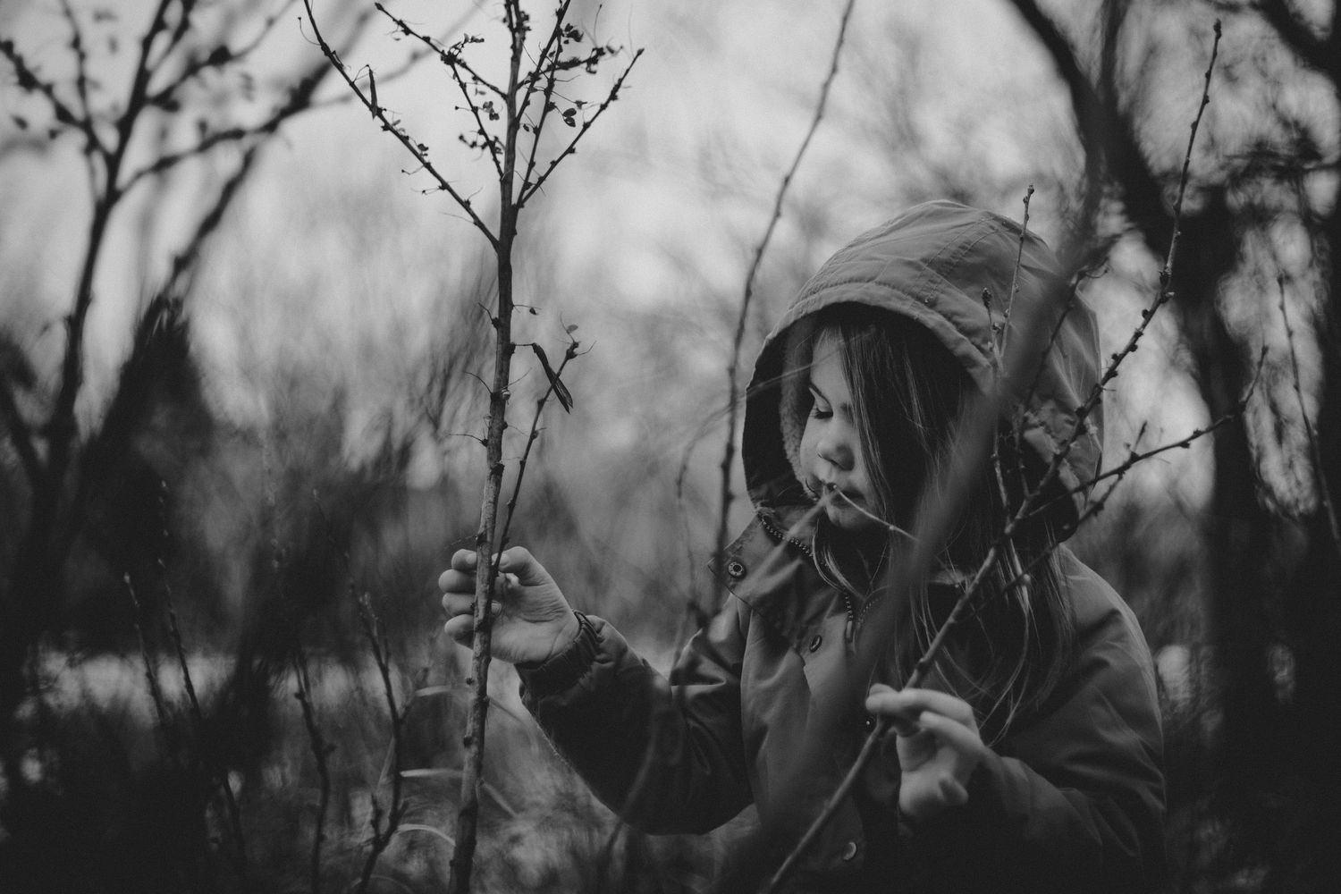 A moody black and white portrait of someone exploring bare winter branches in nature.