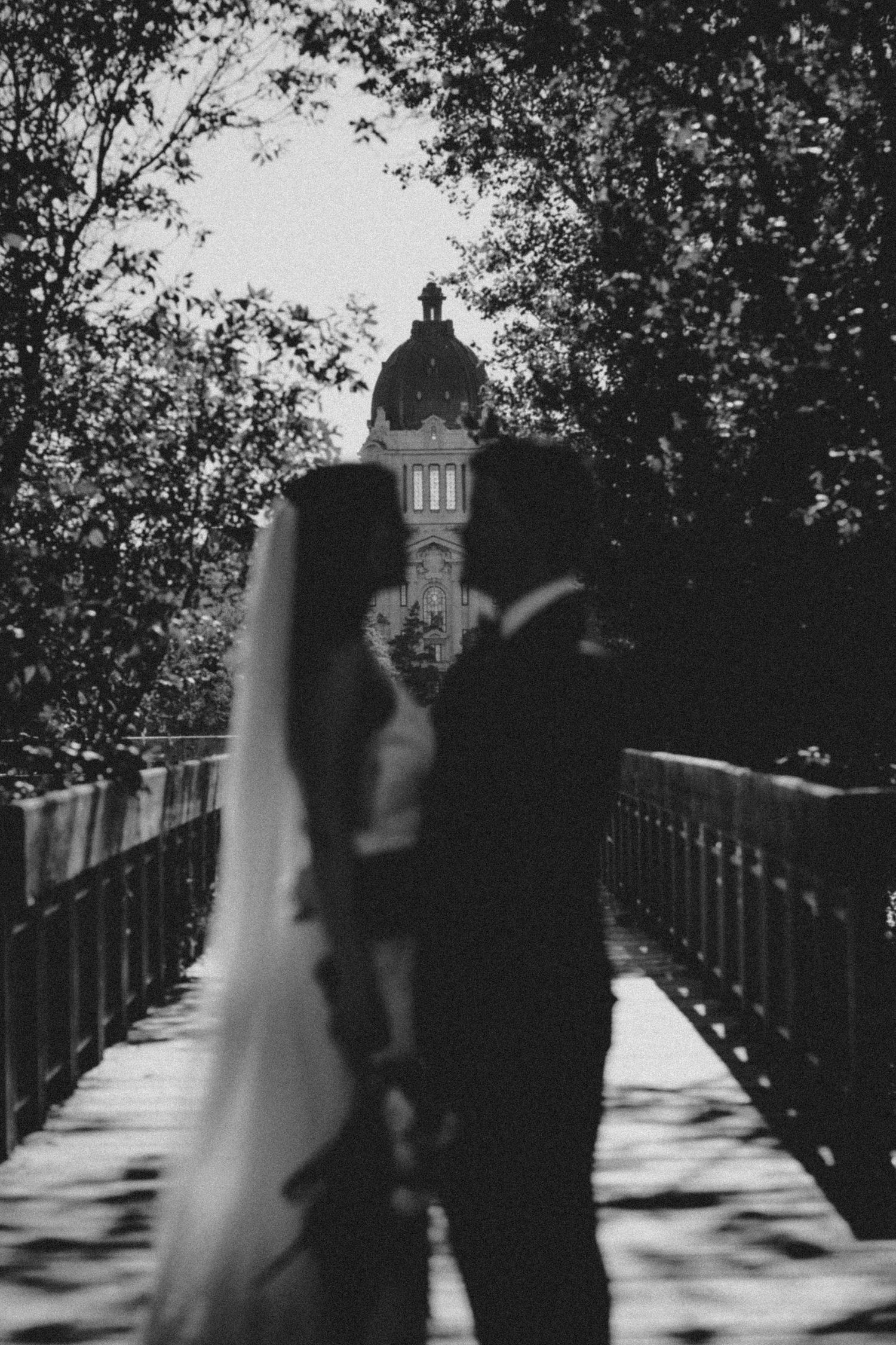 Black and white wedding photo on a bridge with a domed building silhouette in the background.