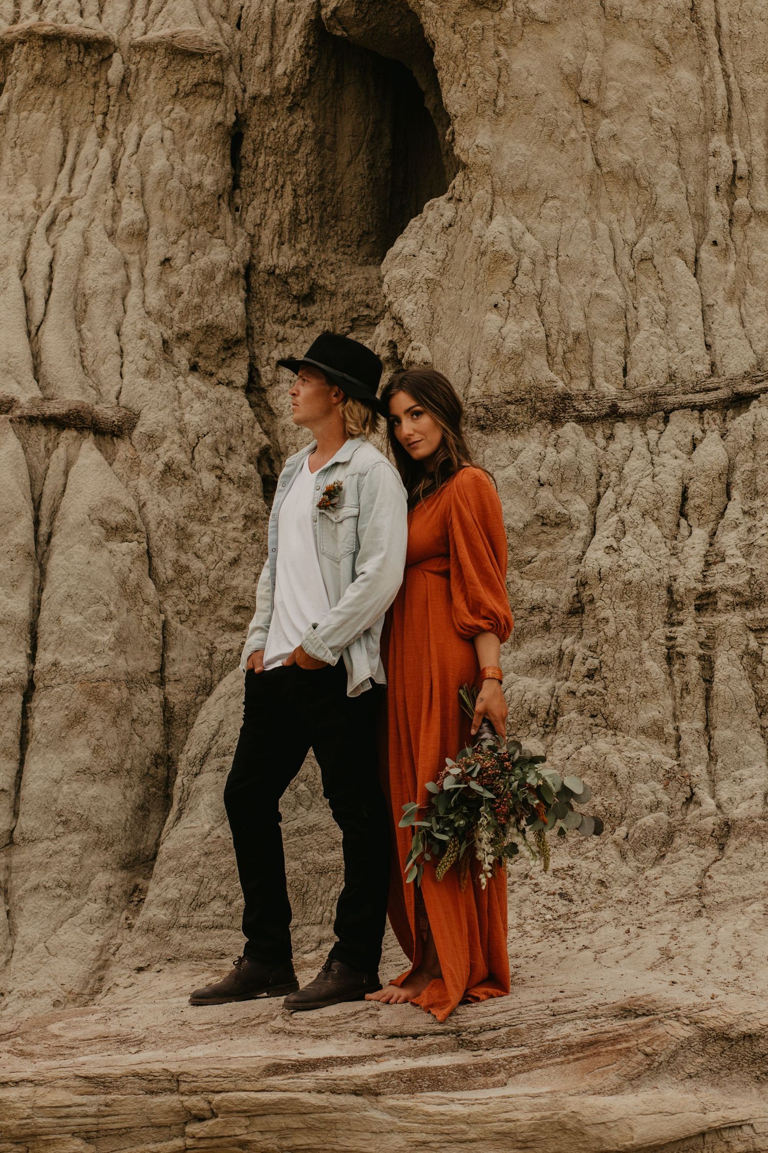 A couple poses against dramatic clay cliffs in boho-style clothing.