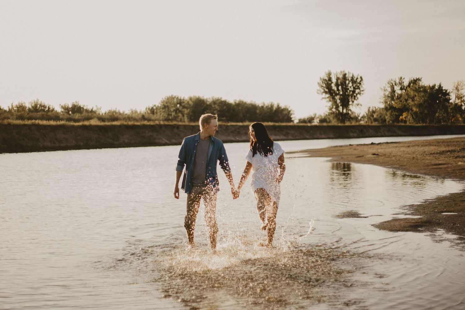 Couple splashes through shallow water while holding hands at sunset.