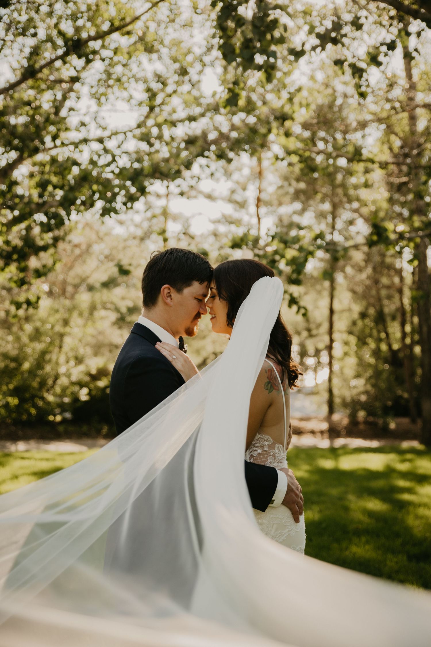 A romantic wedding portrait with flowing veil in a sun-dappled garden setting.