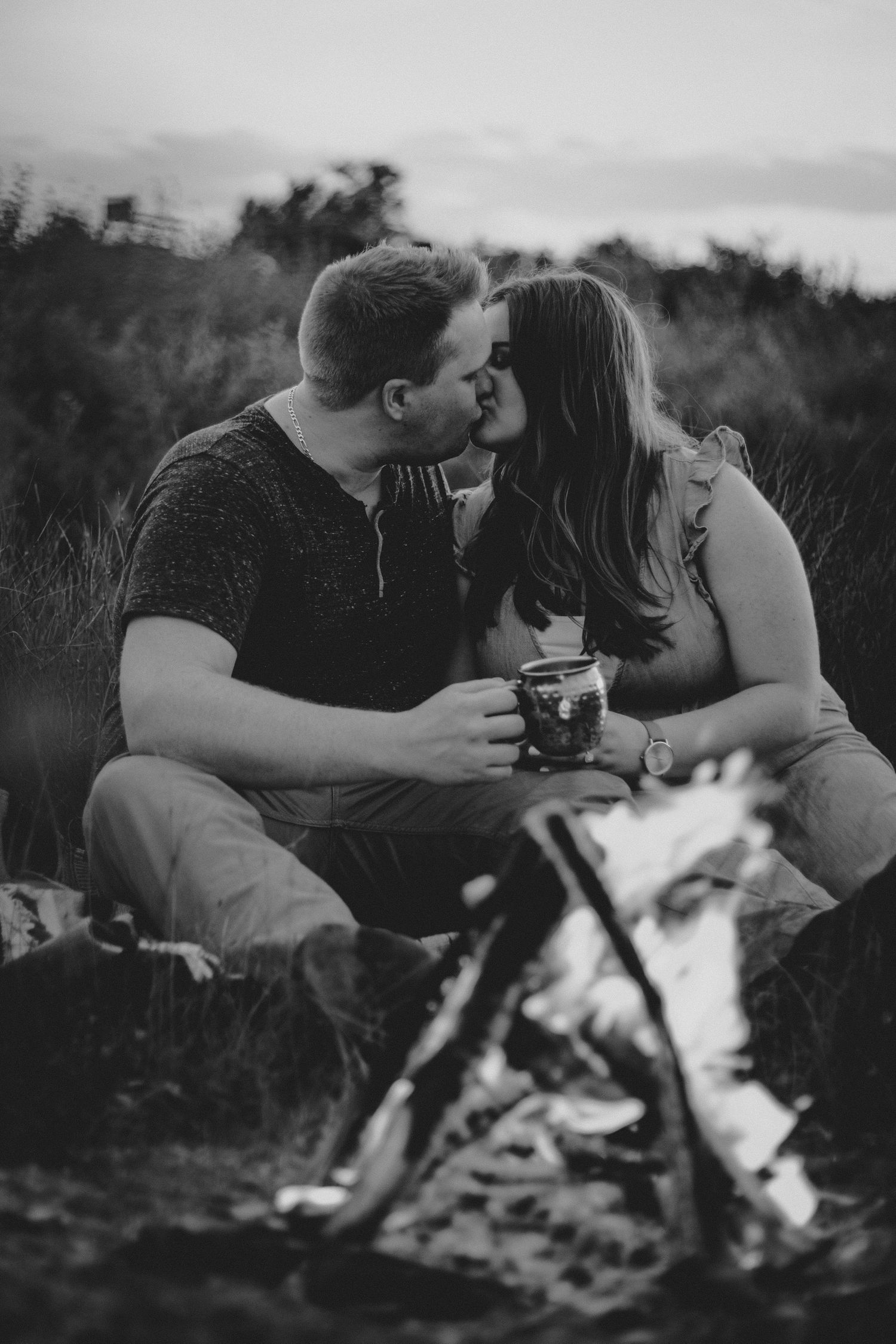 Black and white photo of couple sharing intimate moment by campfire.