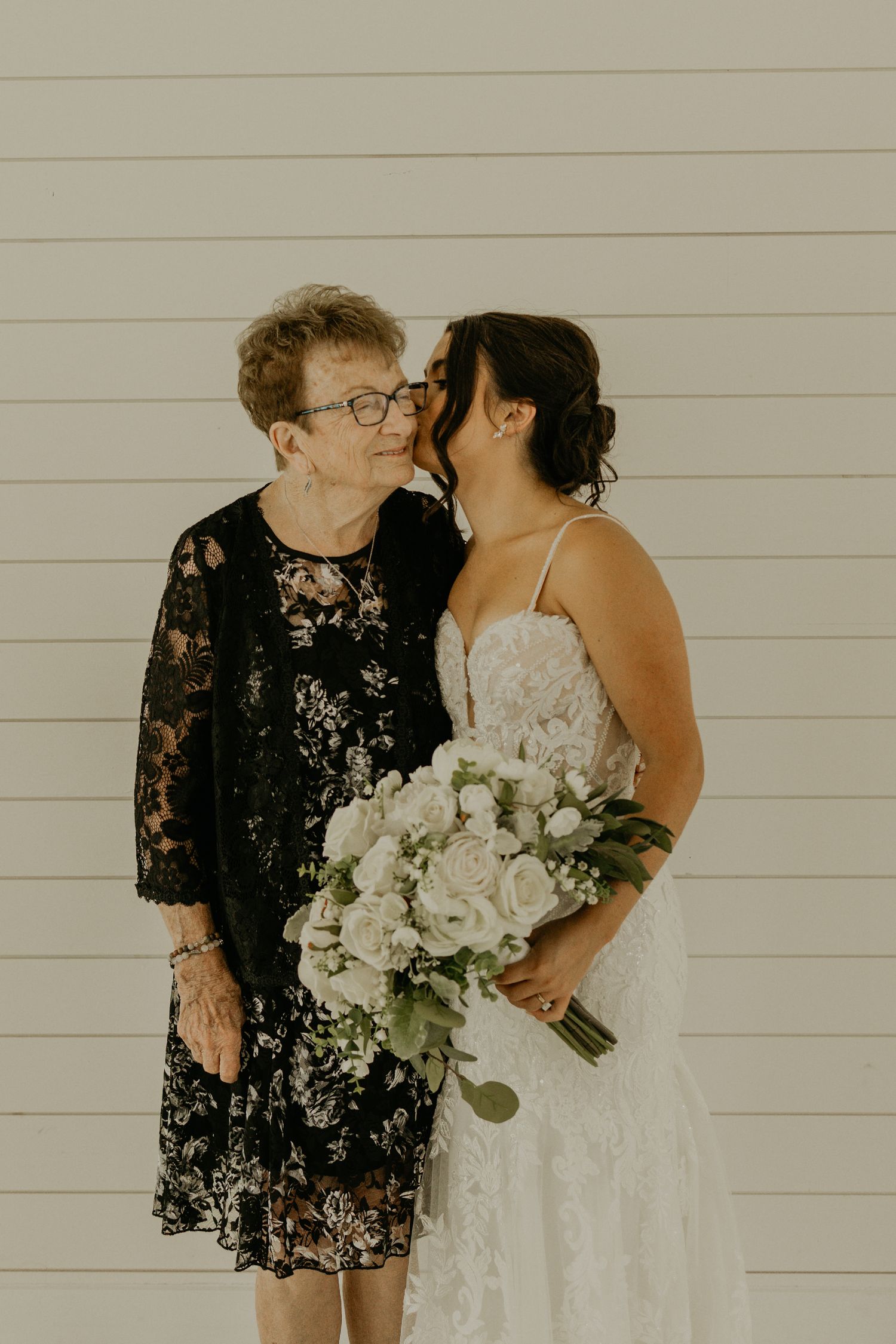 Intimate moment between bride in white lace dress holding bouquet and woman in black lace dress.