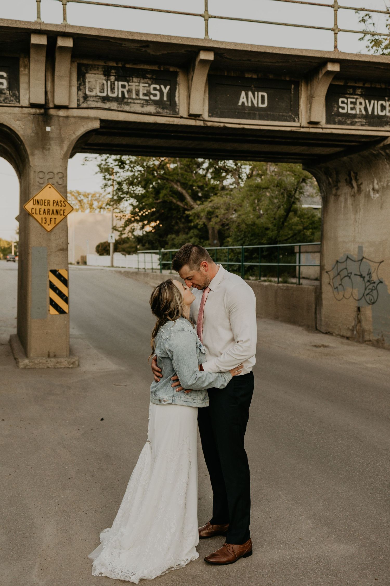 A romantic moment captured under a vintage railway bridge with 'COURTESY AND SERVICE' text overhead.