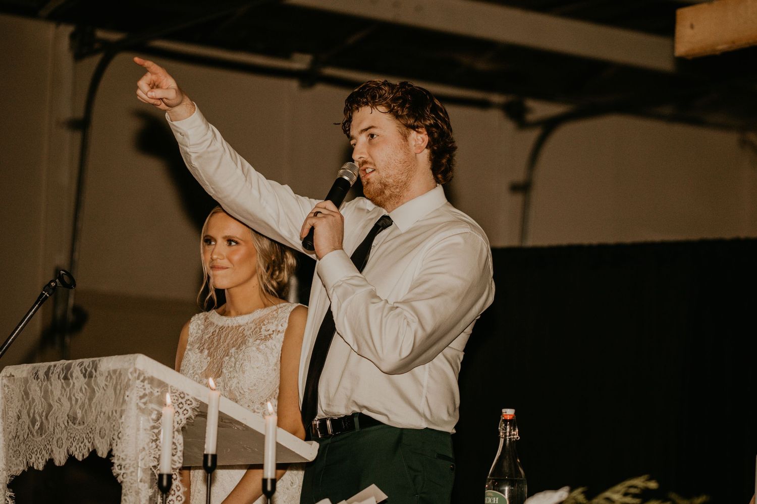 An energetic wedding toast moment at the reception with raised hands and microphone.