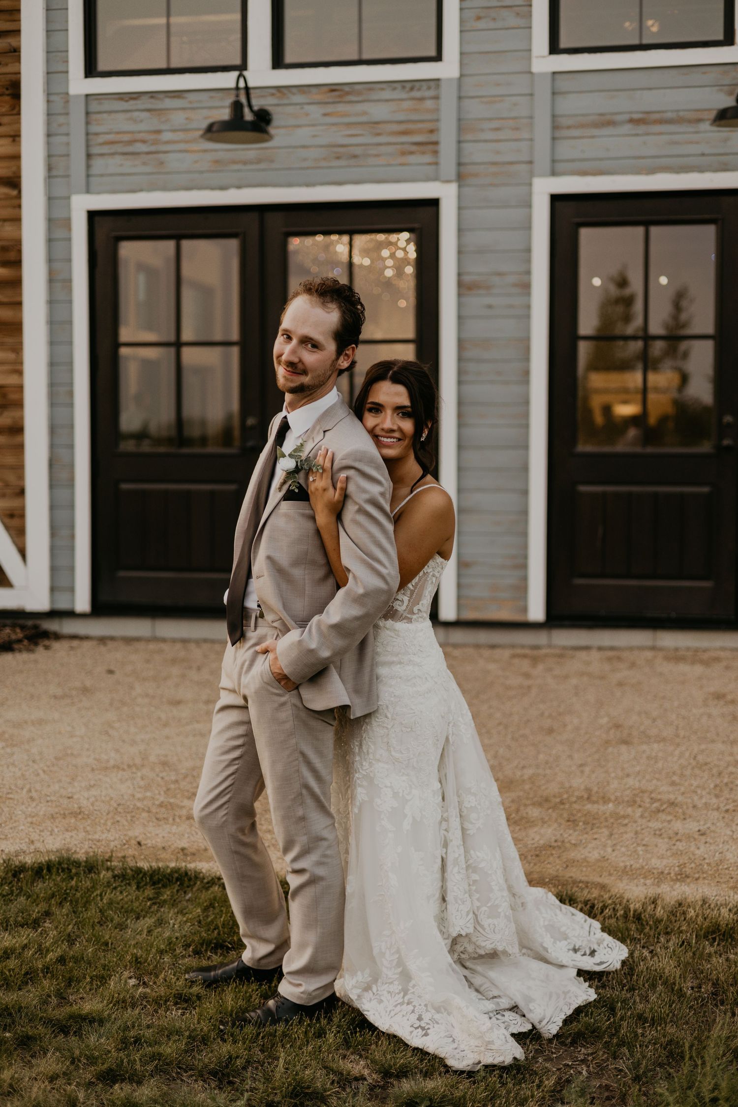 Couple poses playfully back-to-back outside rustic barn wedding venue.