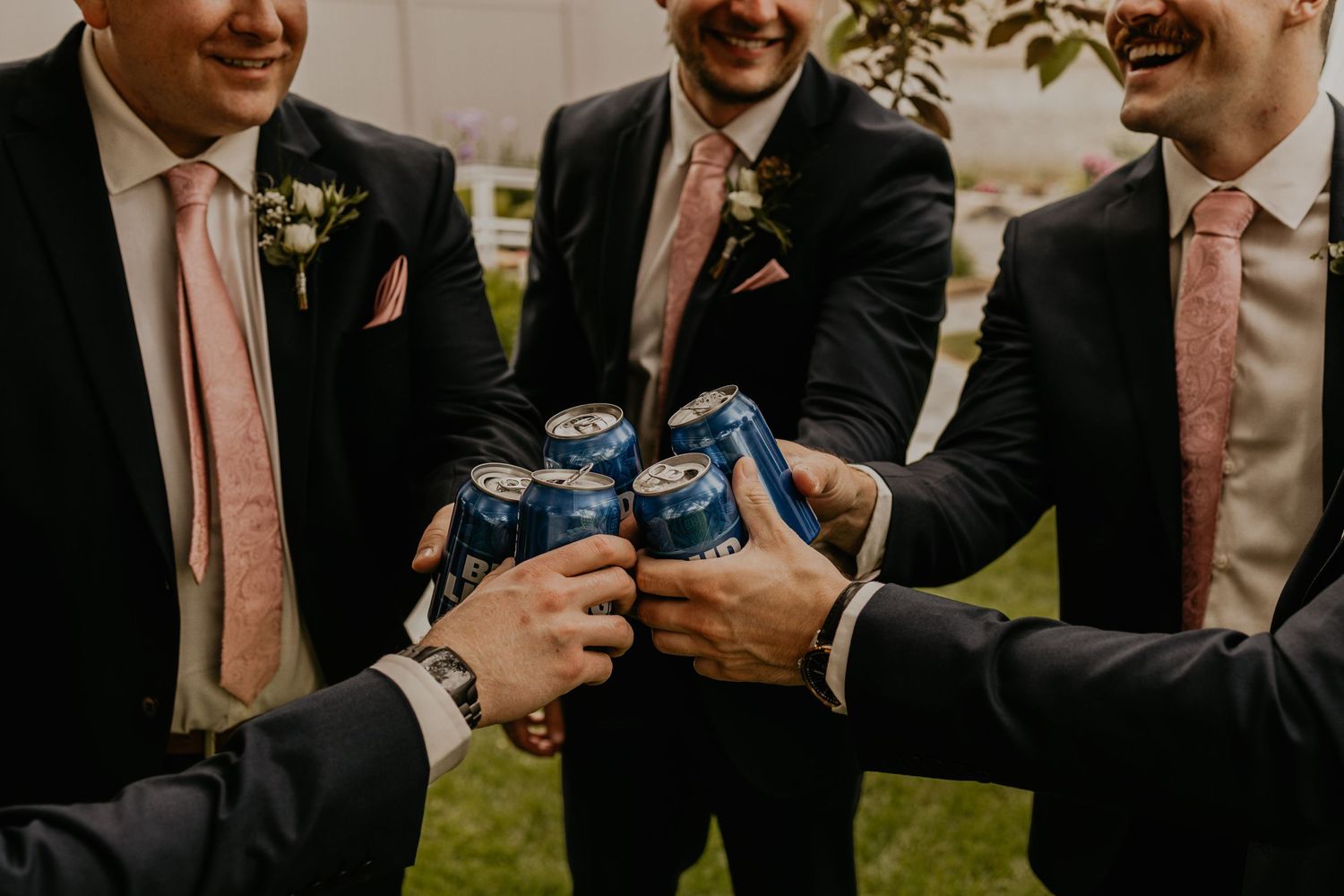Groomsmen toasting with blue bottles during outdoor wedding celebration.
