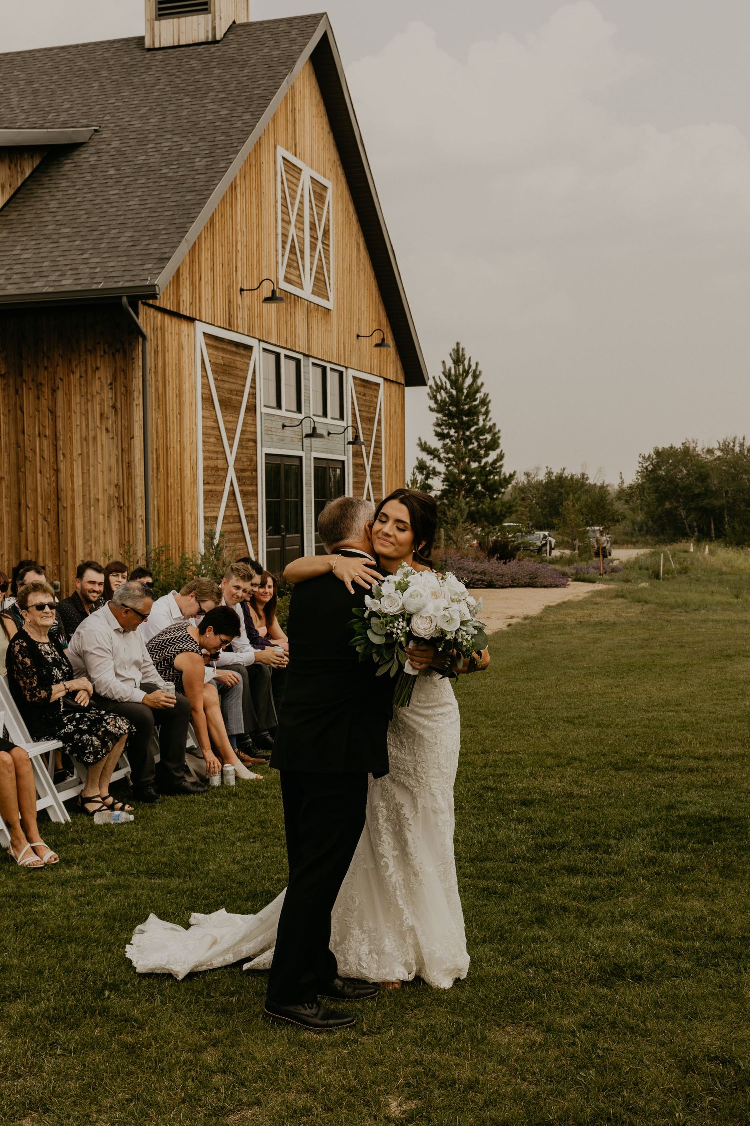 A couple embraces during their wedding ceremony in front of a rustic barn venue.
