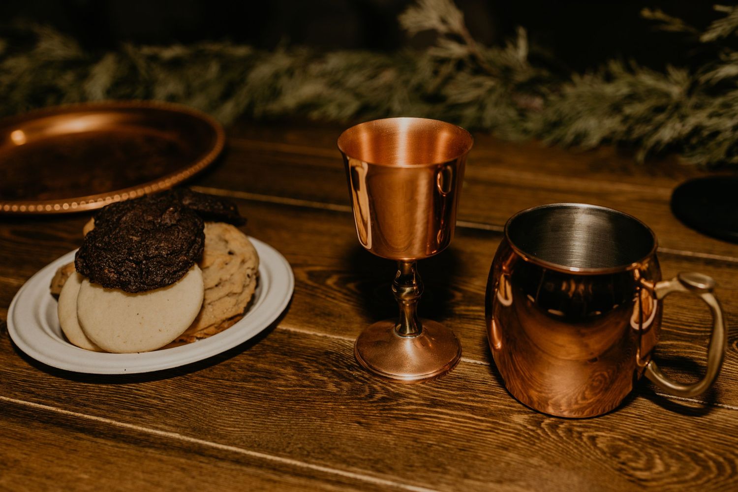 A dessert plate with chocolate treat alongside copper mugs on wooden surface.