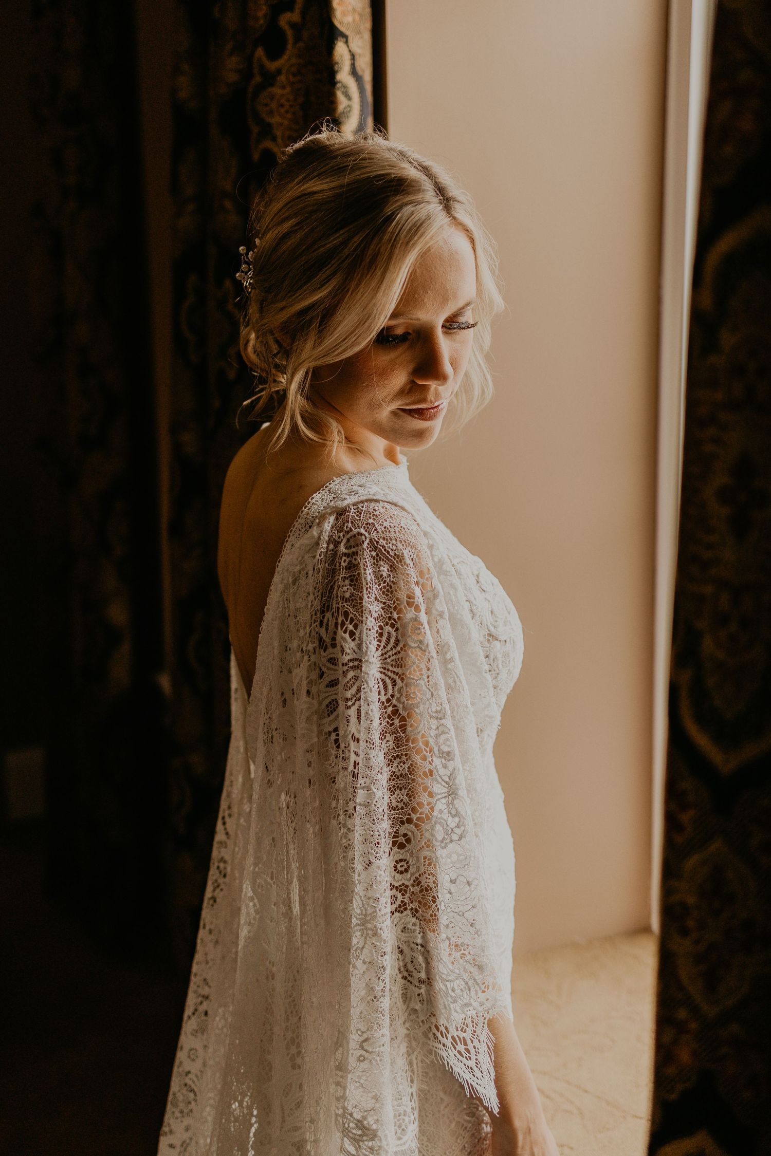 A delicate lace wedding gown is showcased in warm natural window light.
