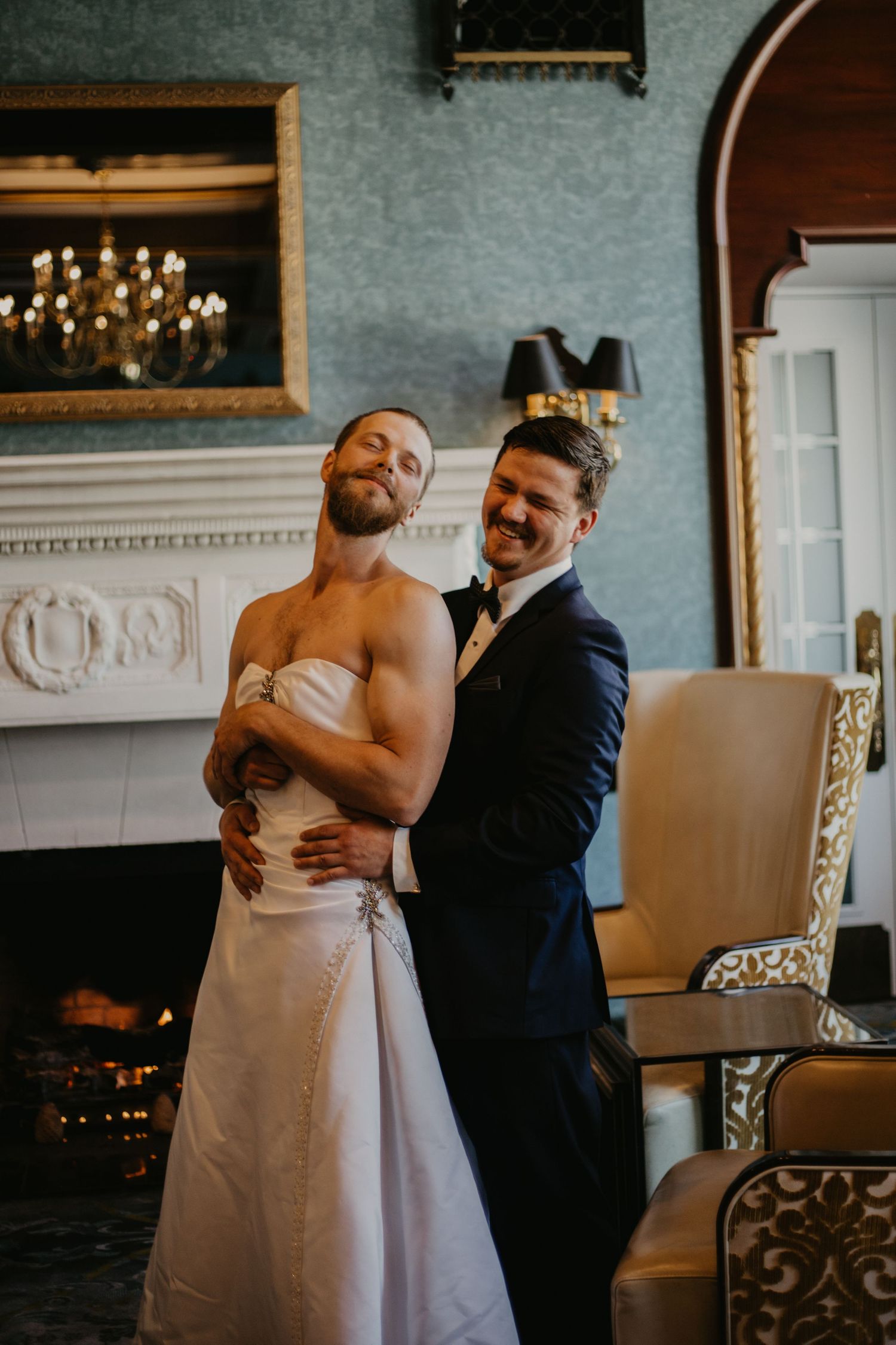 Playful wedding portrait of the couple embracing in front of an ornate fireplace.