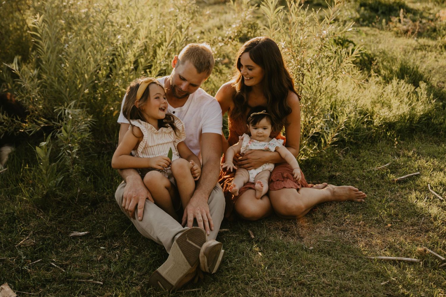 Family lounging together on grassy ground during sunset photo session.