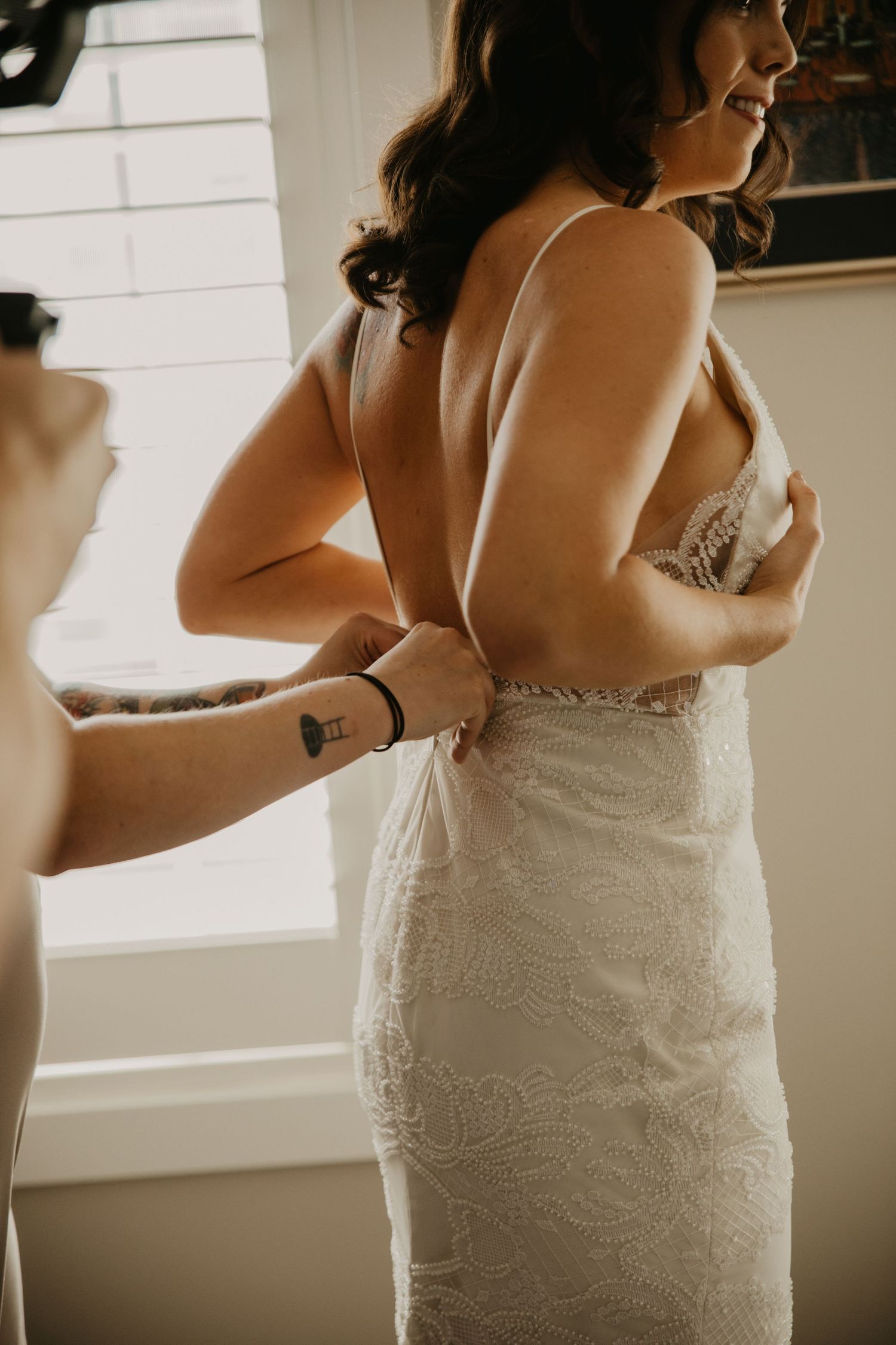 Final adjustments being made to a fitted lace wedding dress during bridal preparations.