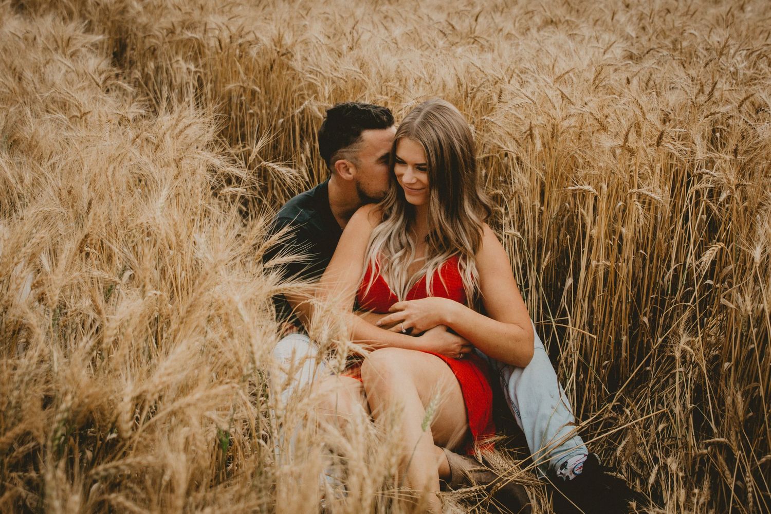 Romantic couple embraces in tall golden wheat field during sunset engagement session.
