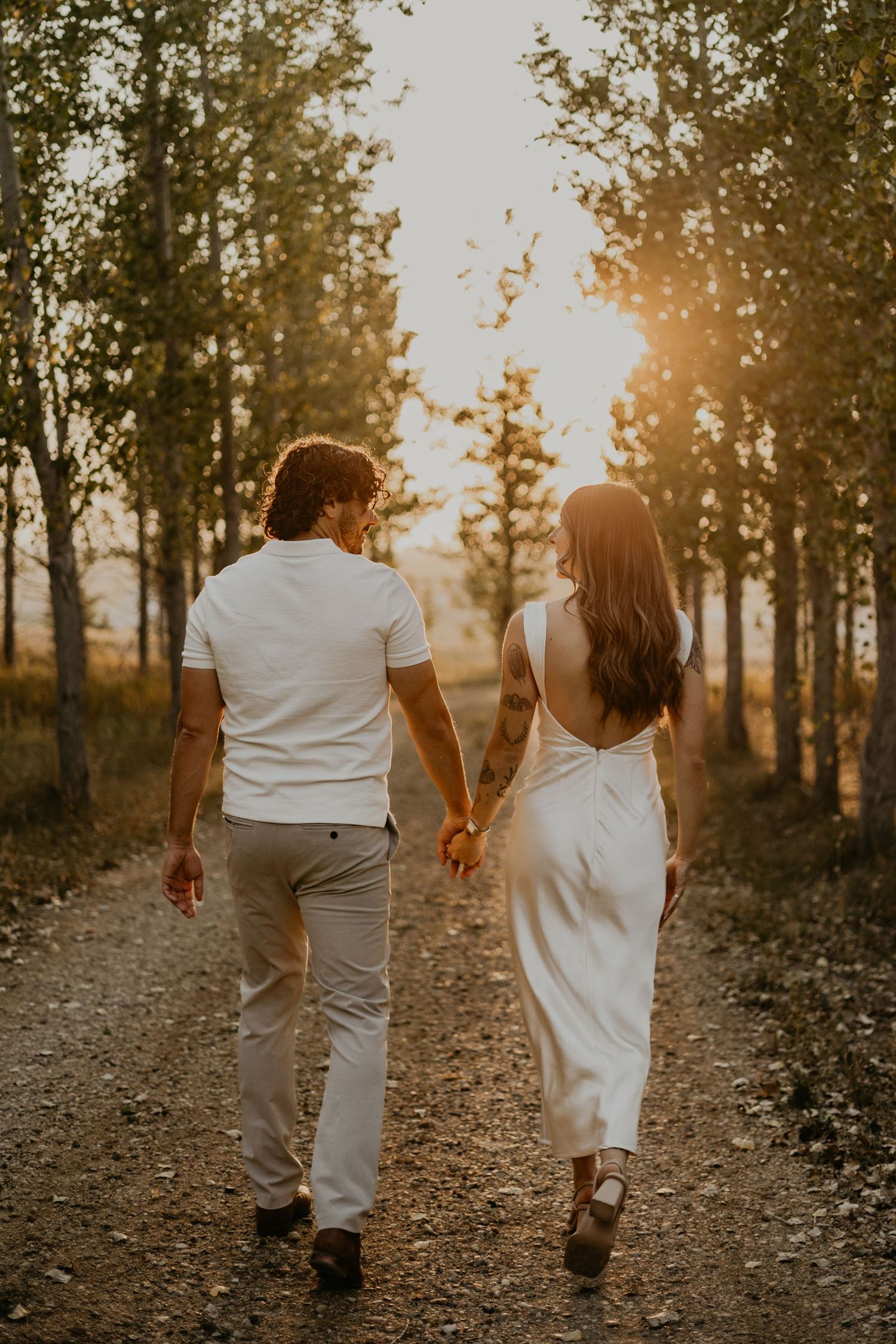 Romantic couple holding hands while walking on a forest path during golden hour.