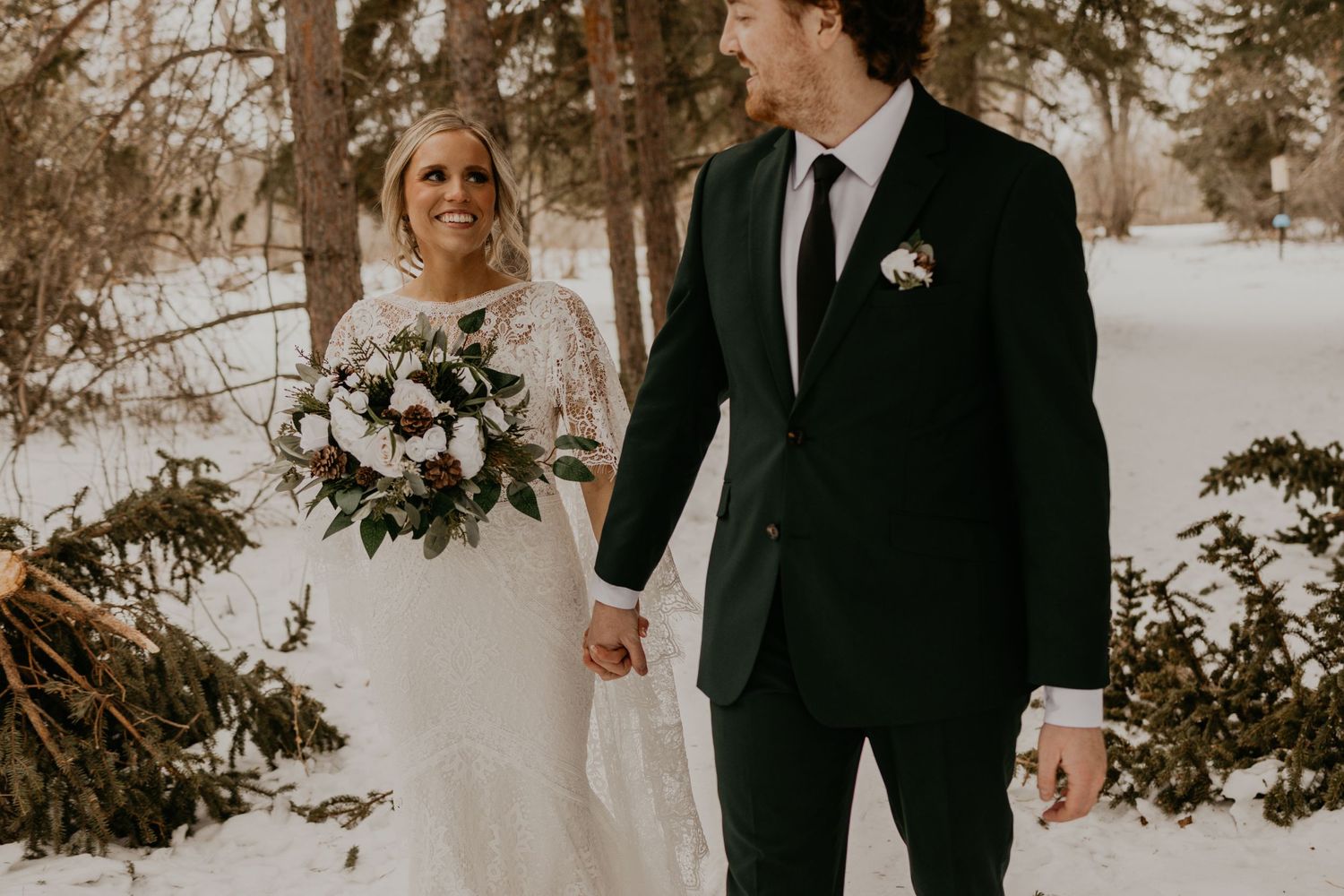 A romantic winter wedding portrait of a couple holding hands in the snow.