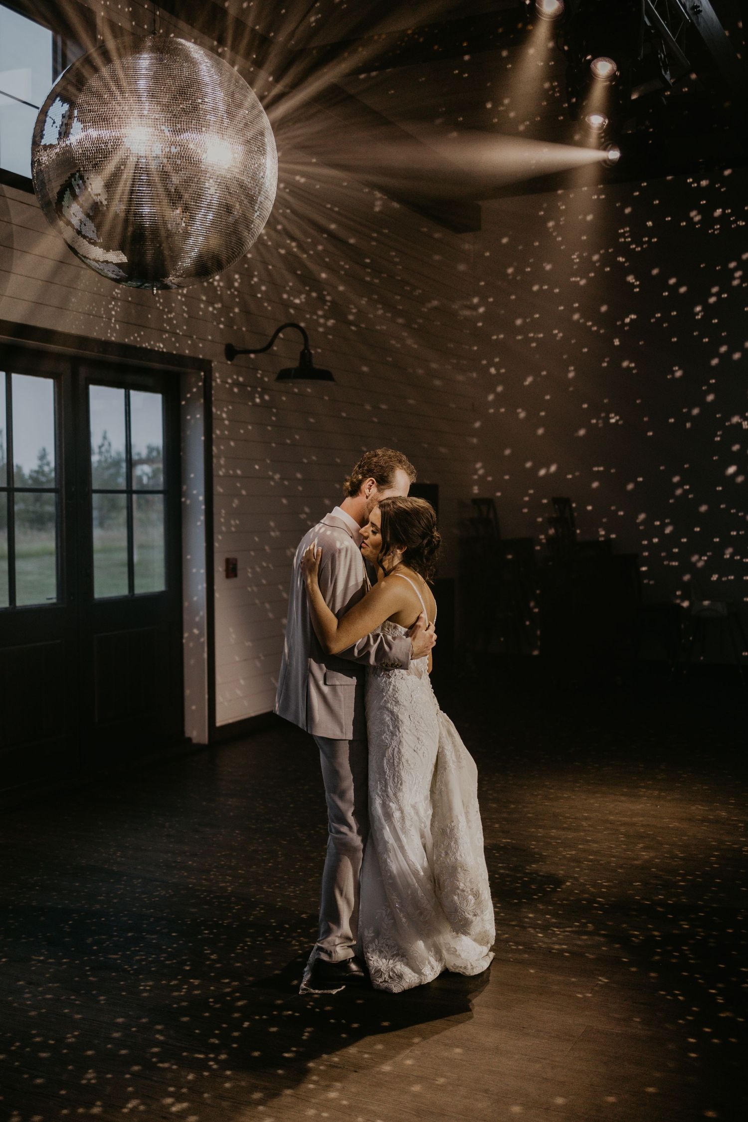 A couple dances under dramatic disco ball lighting creating sparkles throughout the dark reception space.