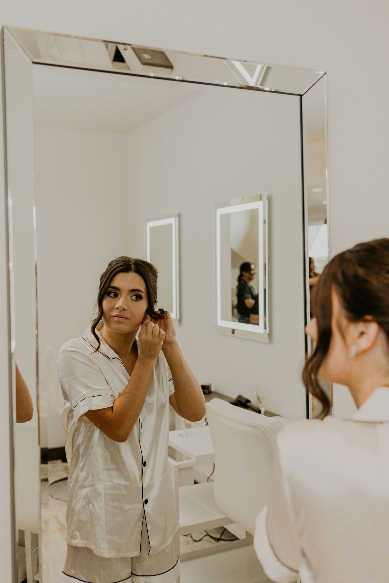 A mirror reflection shows someone applying makeup while wearing white silk pajamas.