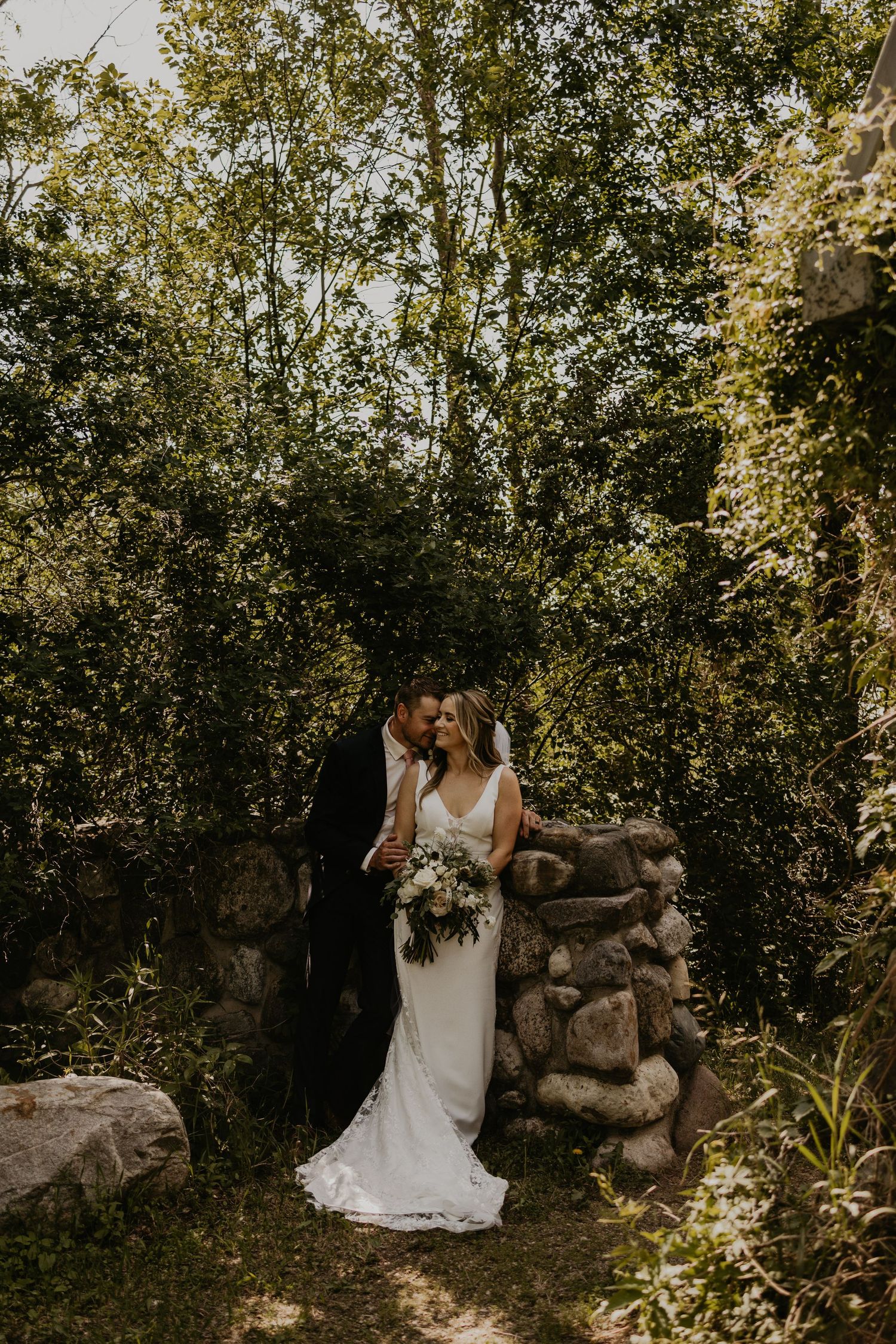 Natural outdoor wedding portrait with couple posed against rustic stone wall.