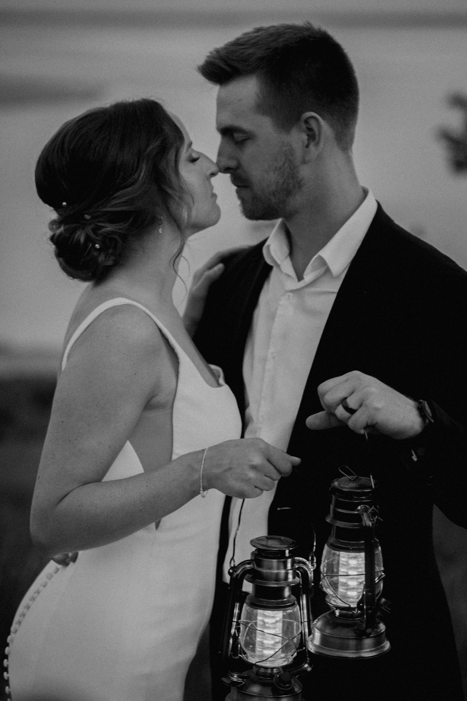 A romantic black and white portrait of a couple about to kiss while holding vintage lanterns.