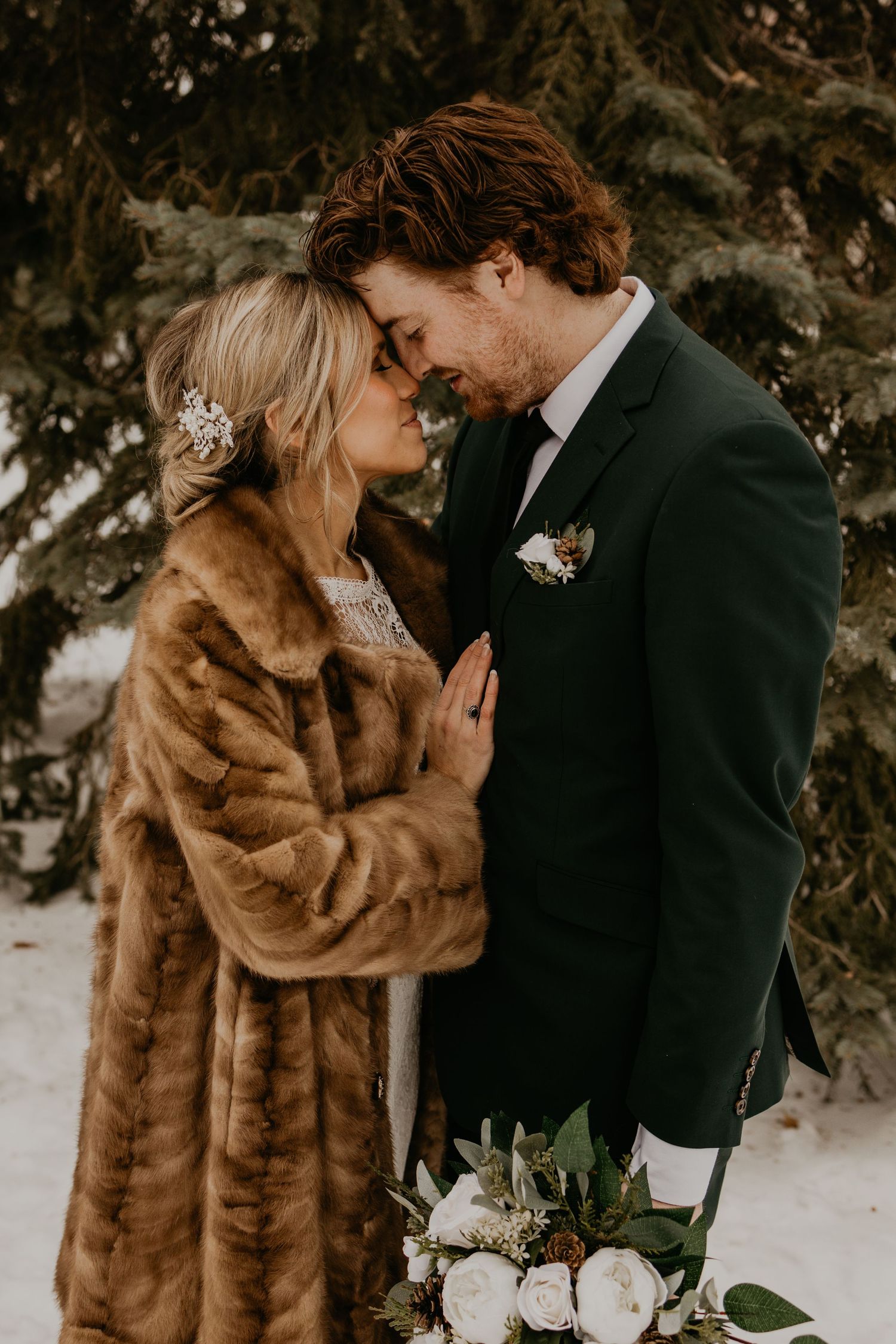 Intimate winter wedding moment between couple in fur coat and black suit with white floral bouquet.