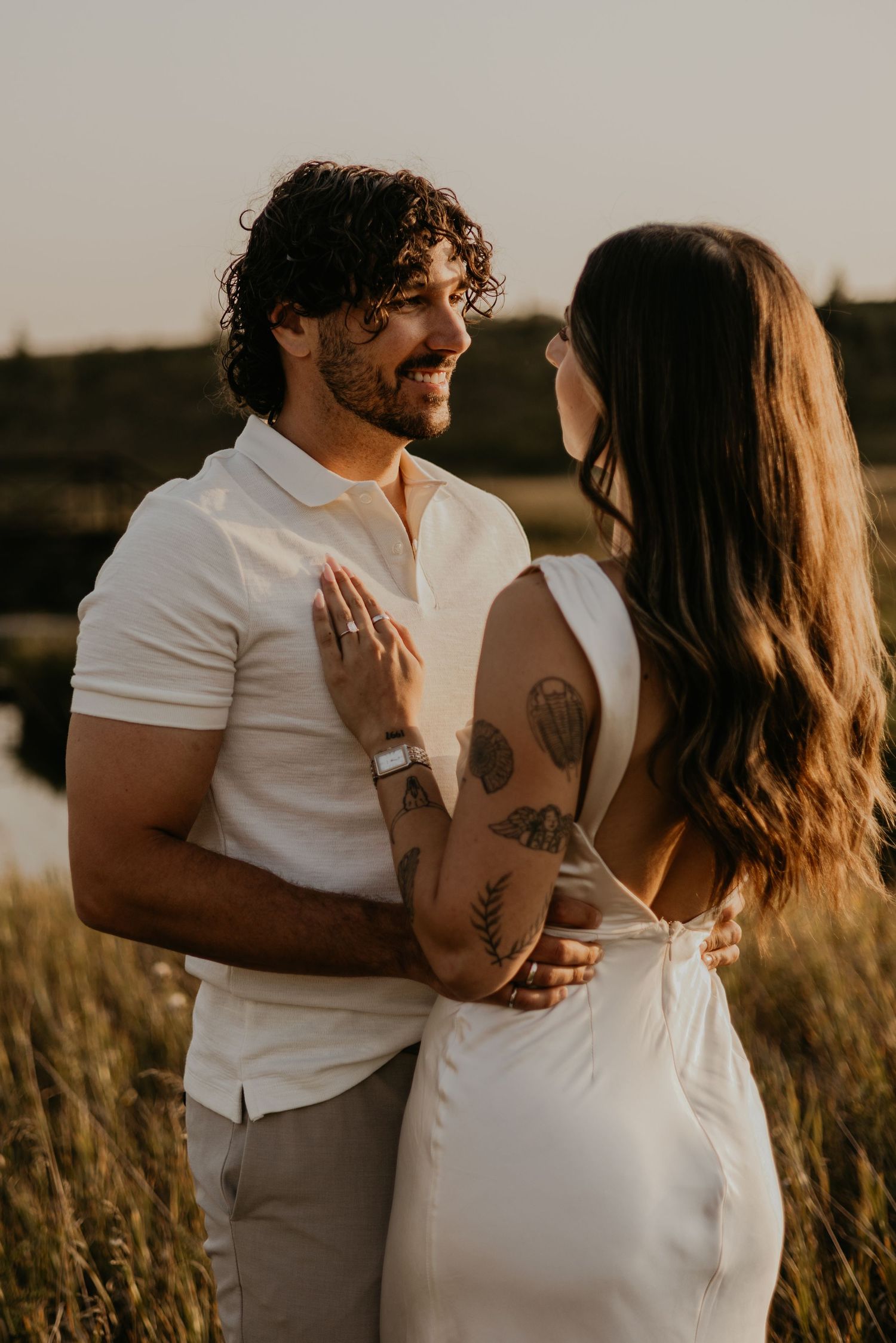Couple sharing a tender moment in tall grass during golden hour at sunset.