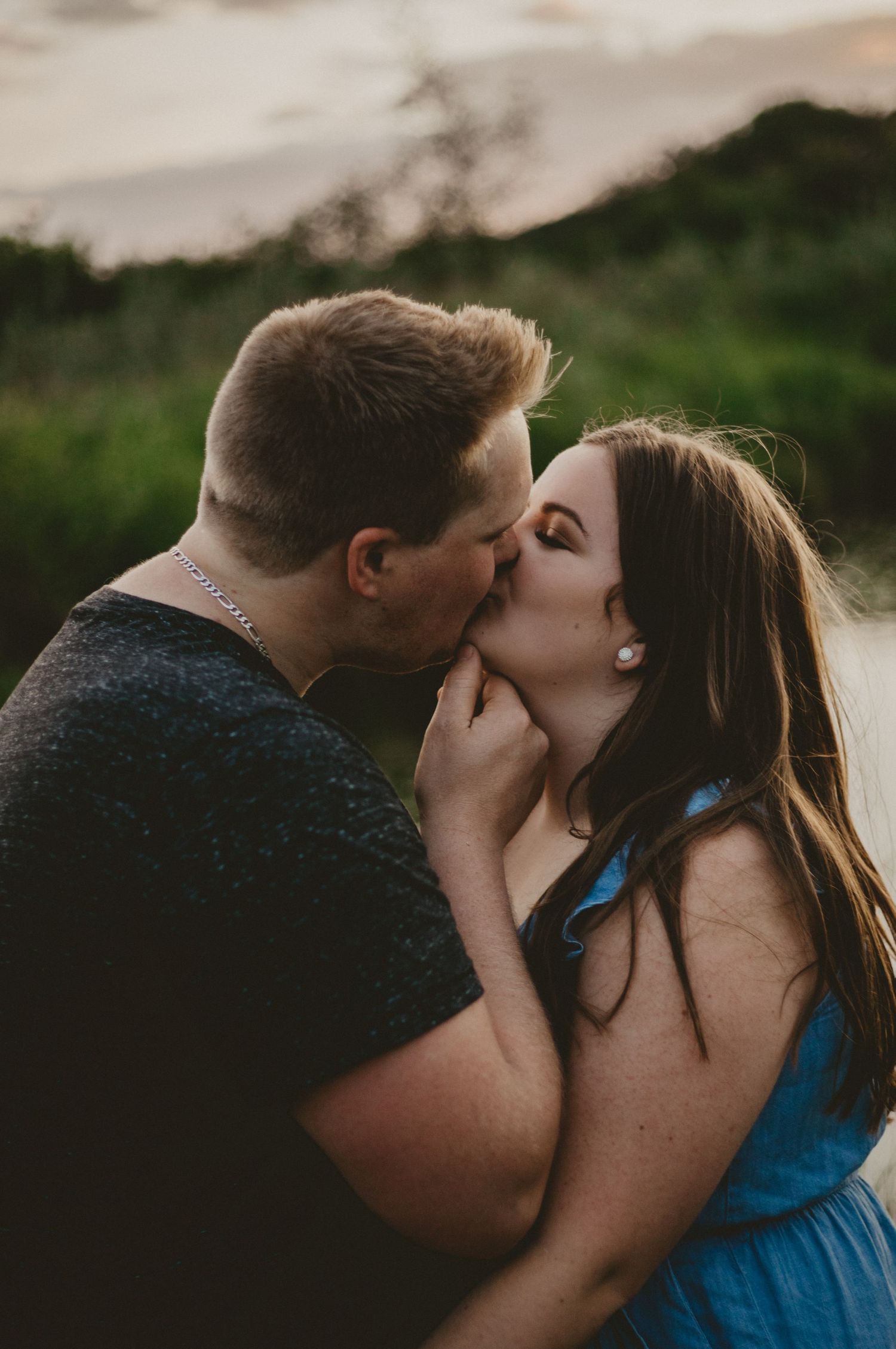 Romantic couple sharing an intimate kiss at sunset in a natural outdoor setting.