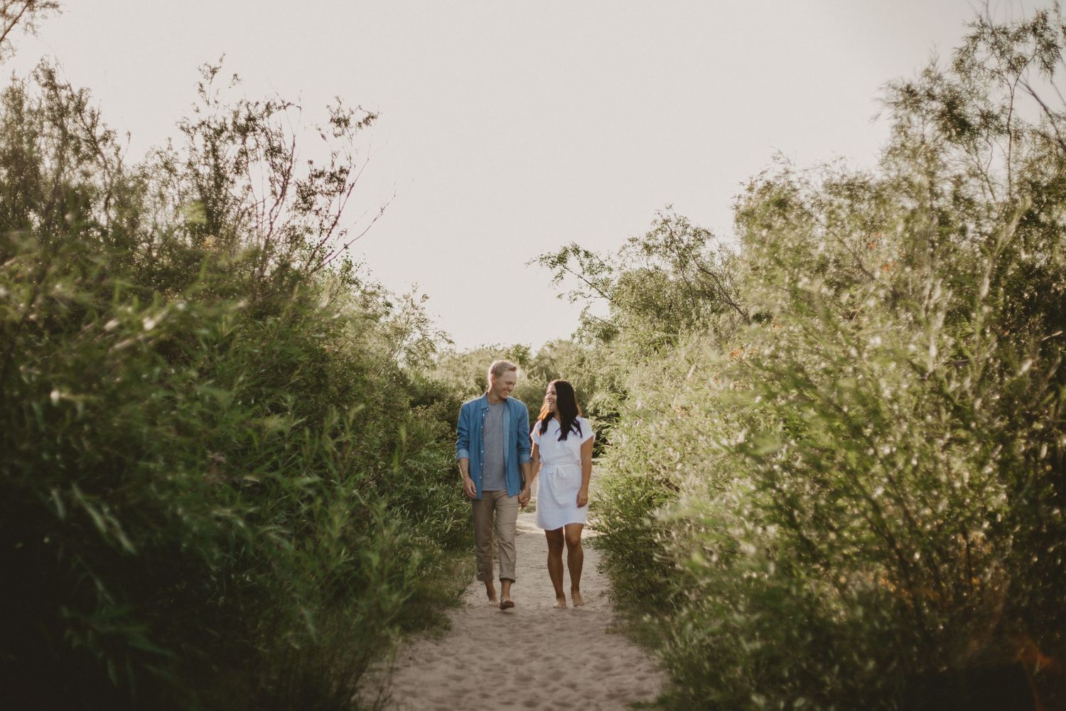 Couple walking hand in hand down a nature path surrounded by green foliage.