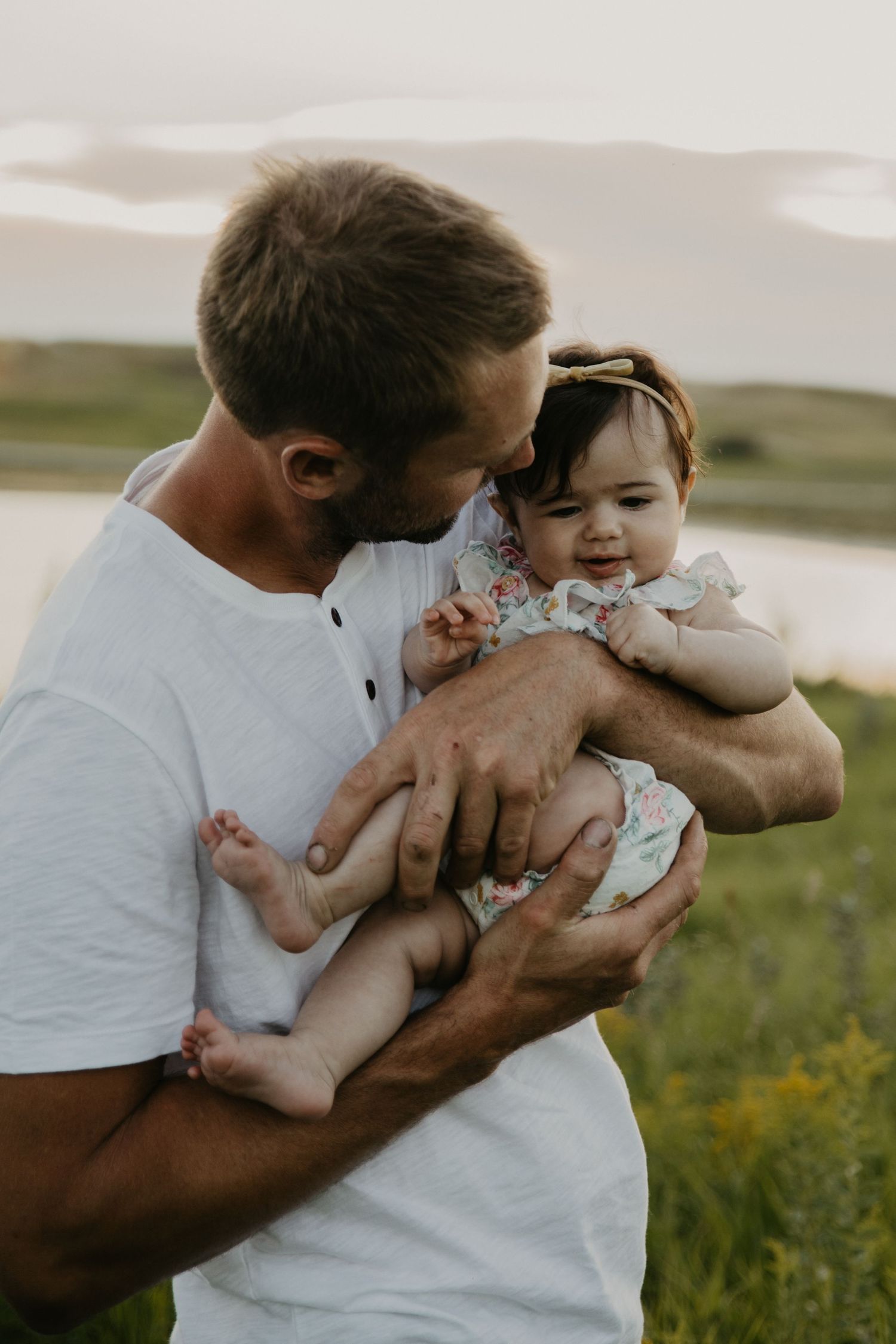 Tender moment between adult and infant in floral outfit against natural landscape.