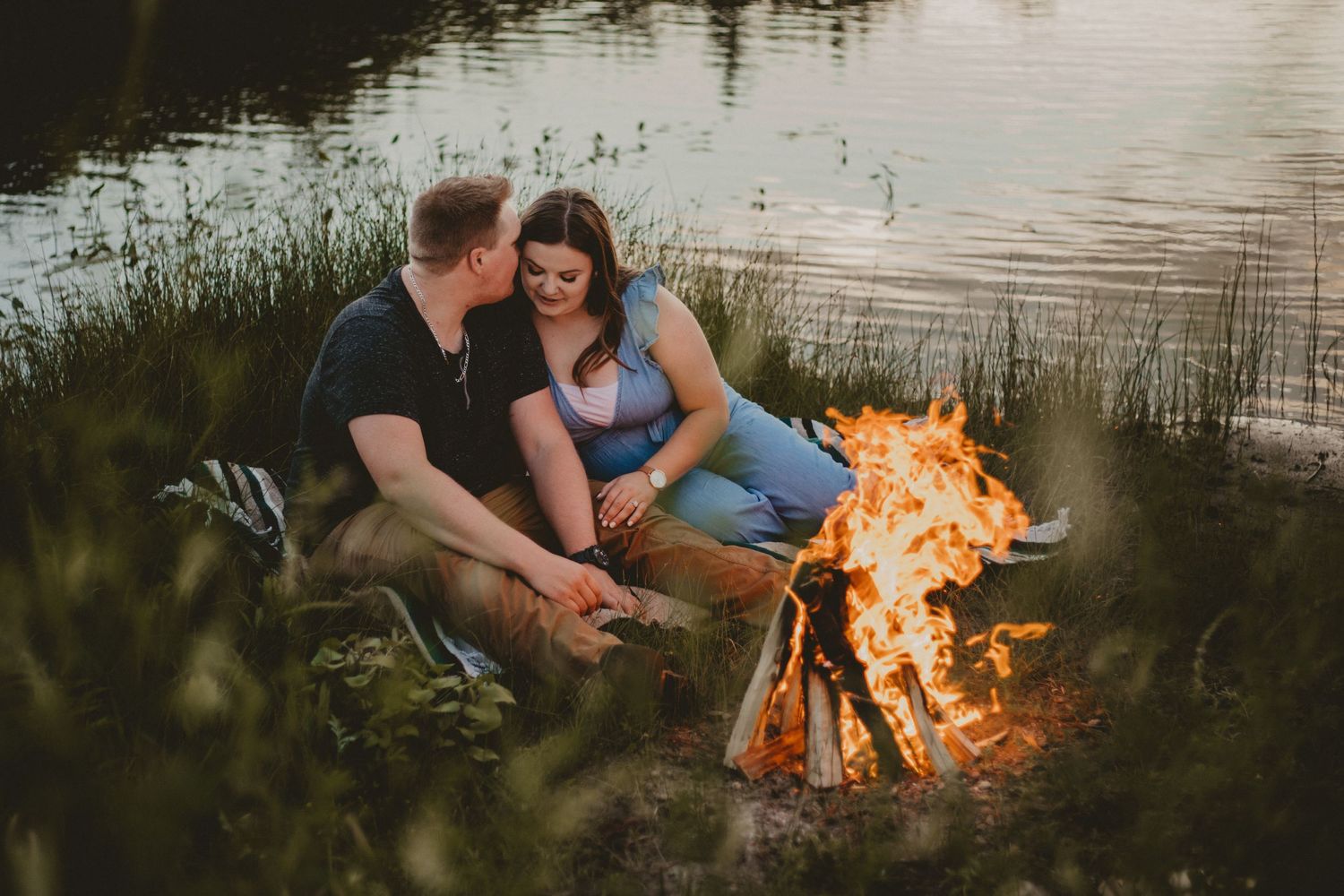 A couple enjoys a romantic evening by a lakeside campfire.