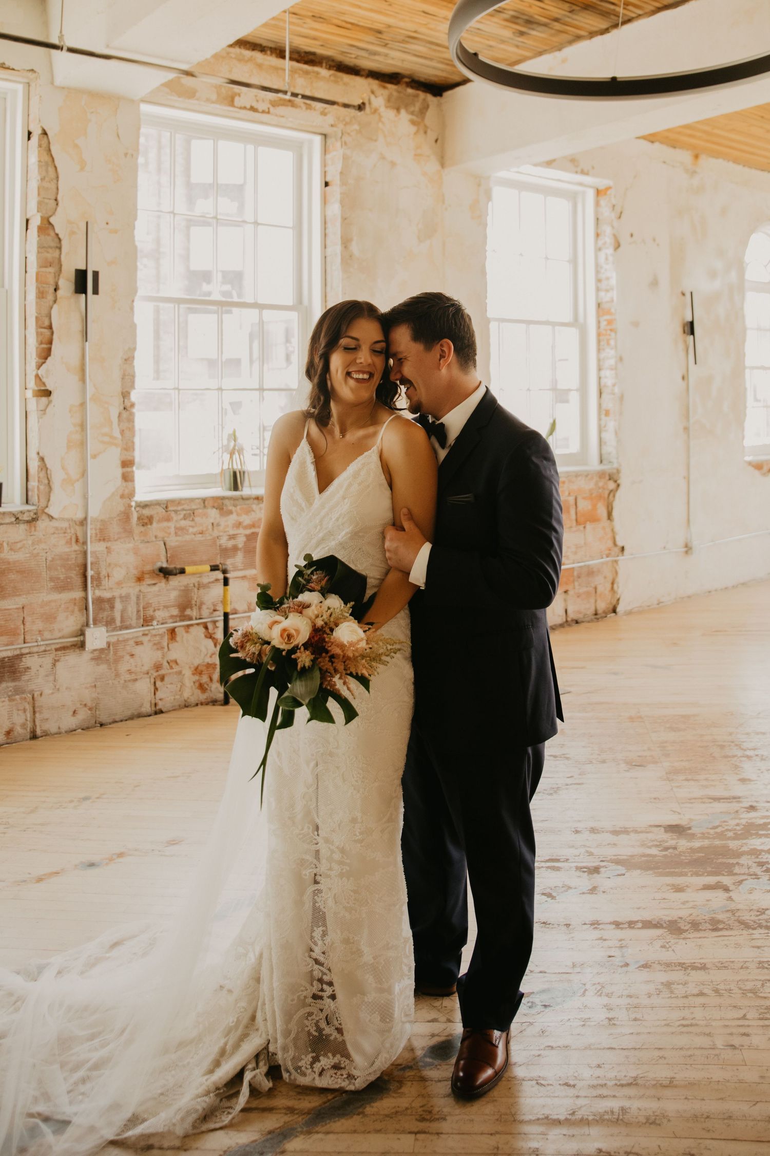 A newlywed couple shares an intimate moment in a rustic brick-walled venue.