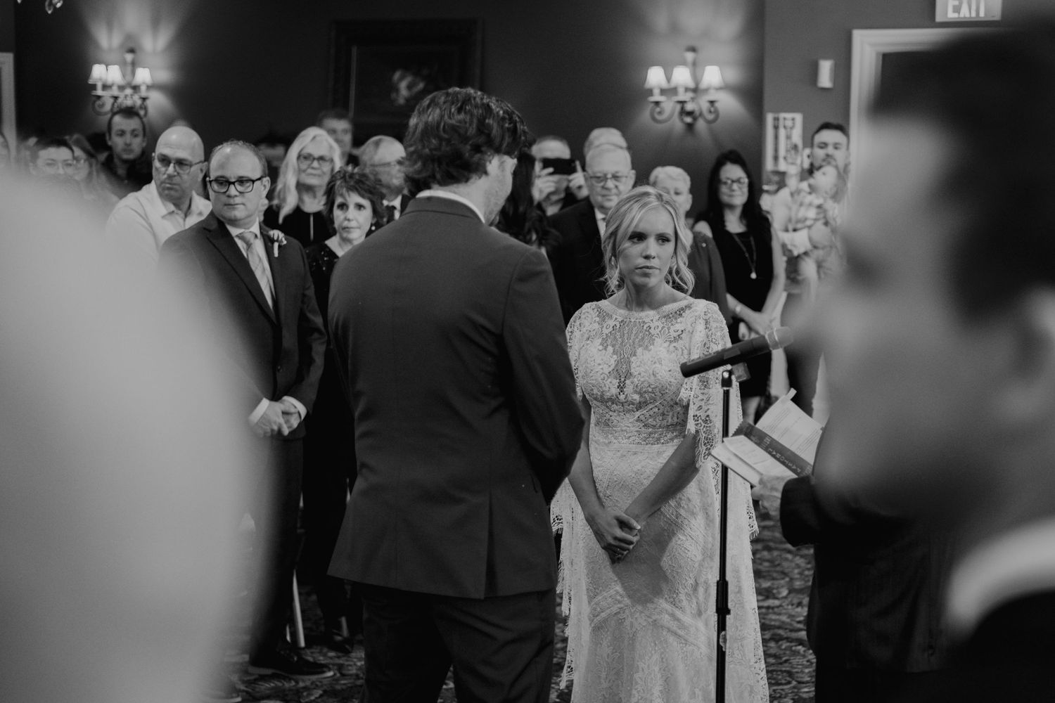 Black and white photo of wedding ceremony with guests watching in formal attire.
