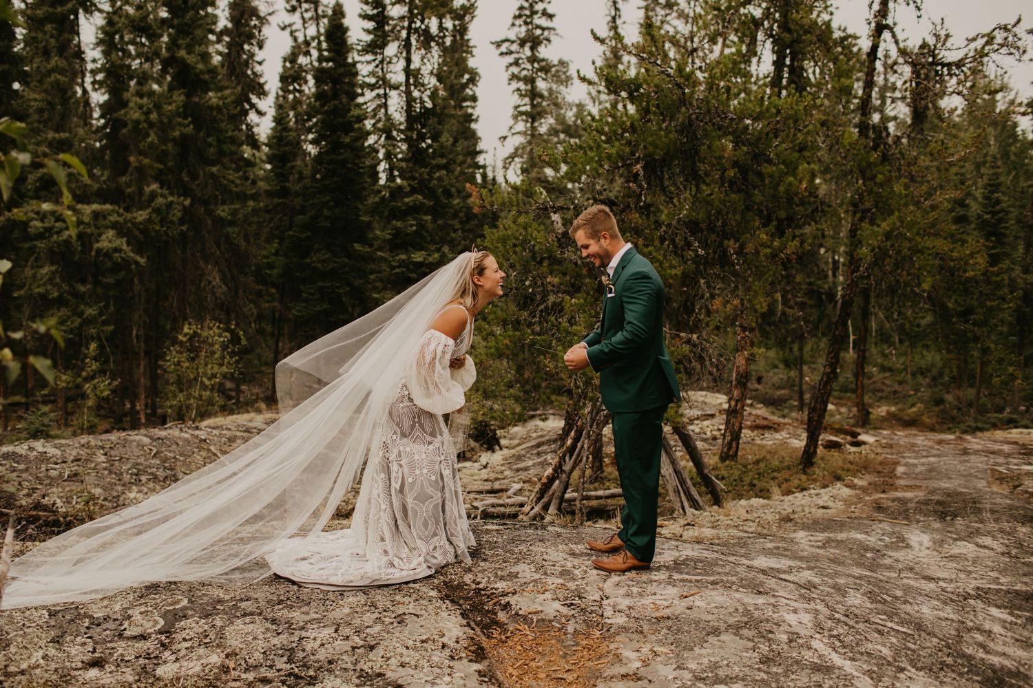 Wedding ceremony on rocky mountain ledge with pine forest backdrop and flowing veil.