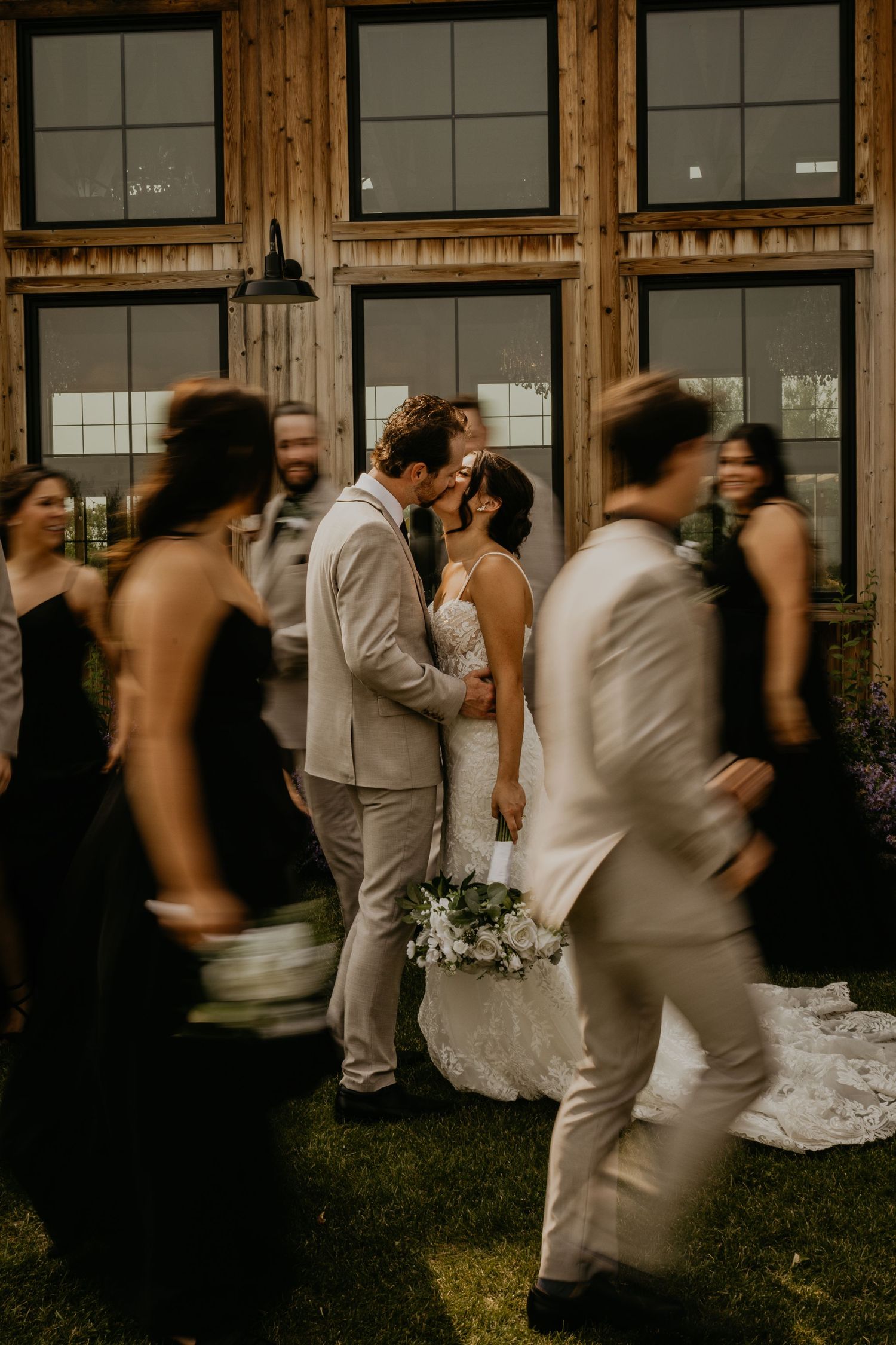 Wedding party in motion with couple sharing moment while others dance through outdoor venue.