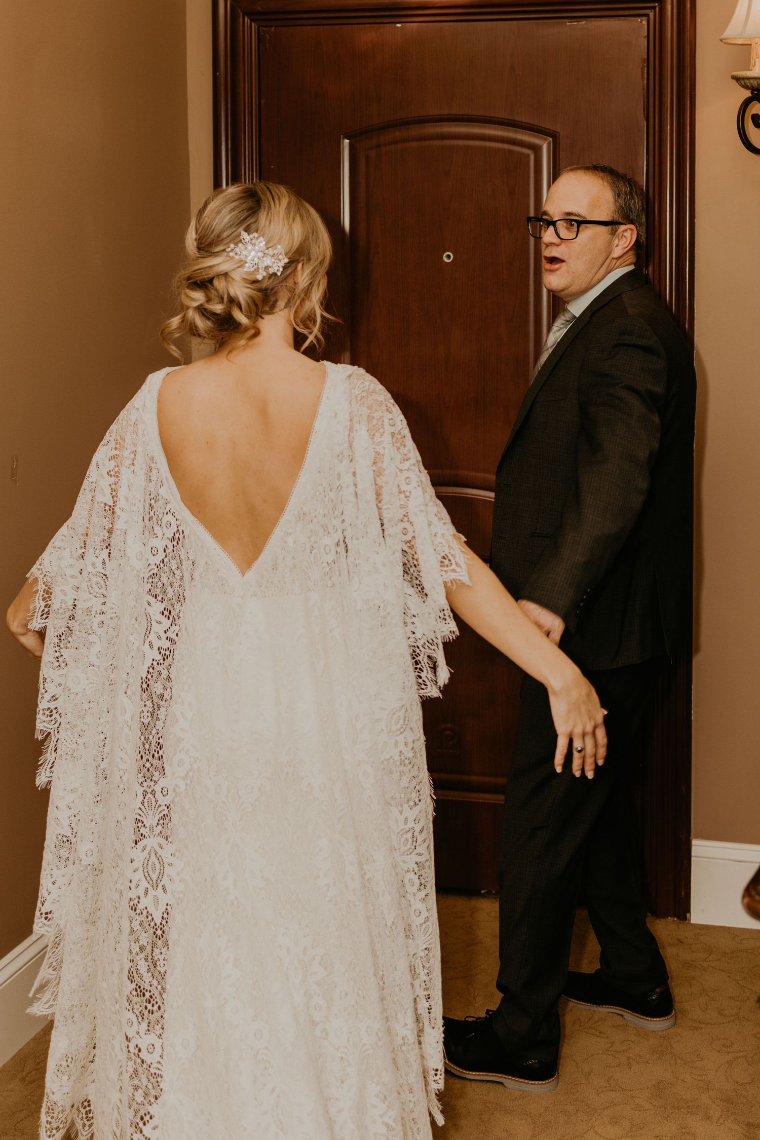A wedding dress with delicate lace details and flowing cape sleeves seen from behind.