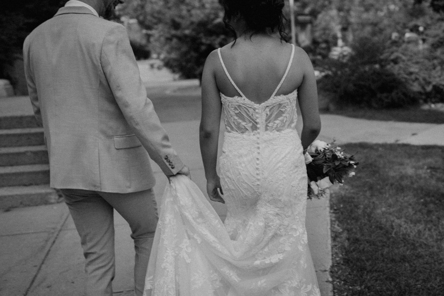 Black and white photo of couple walking together showing lace wedding dress detail.