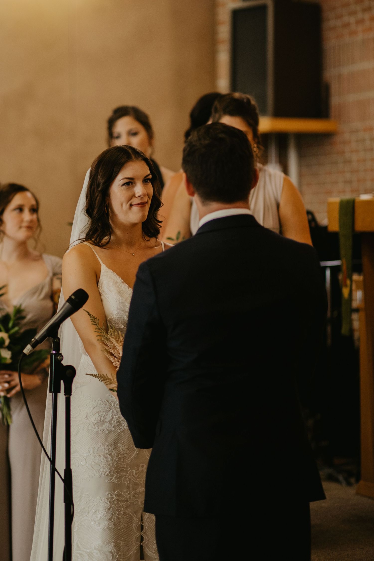An intimate wedding ceremony moment in a rustic brick-walled venue with natural lighting.