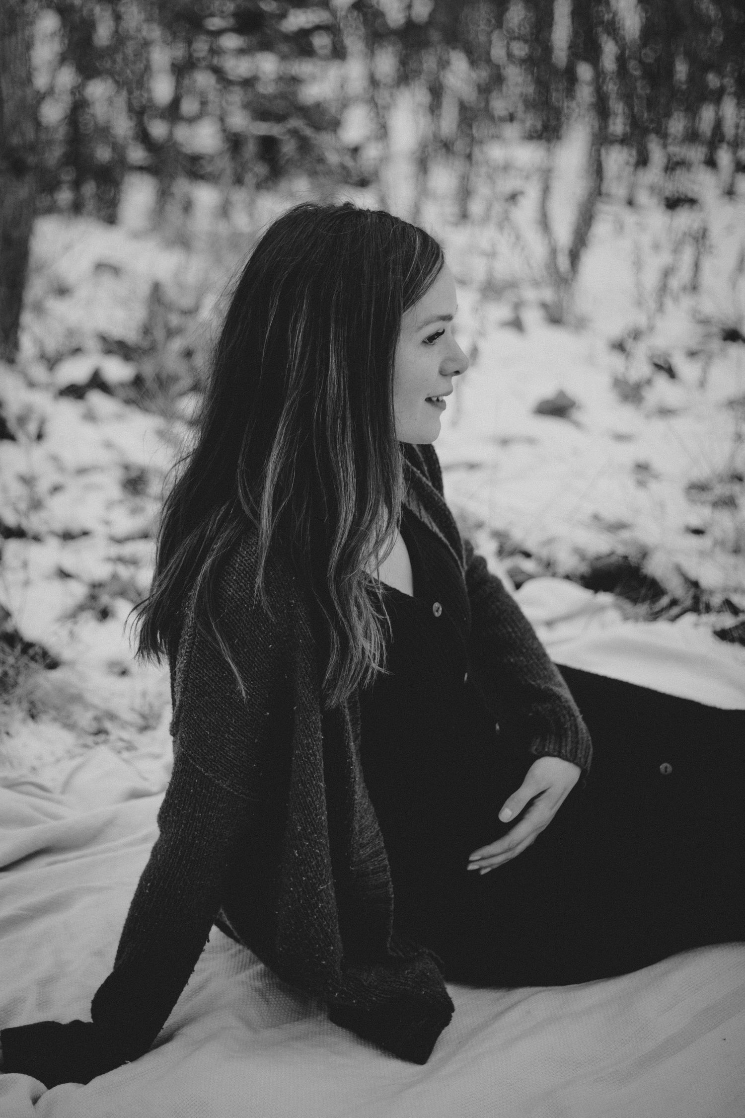 A person laughs while sitting in the snow during a black and white winter photoshoot.