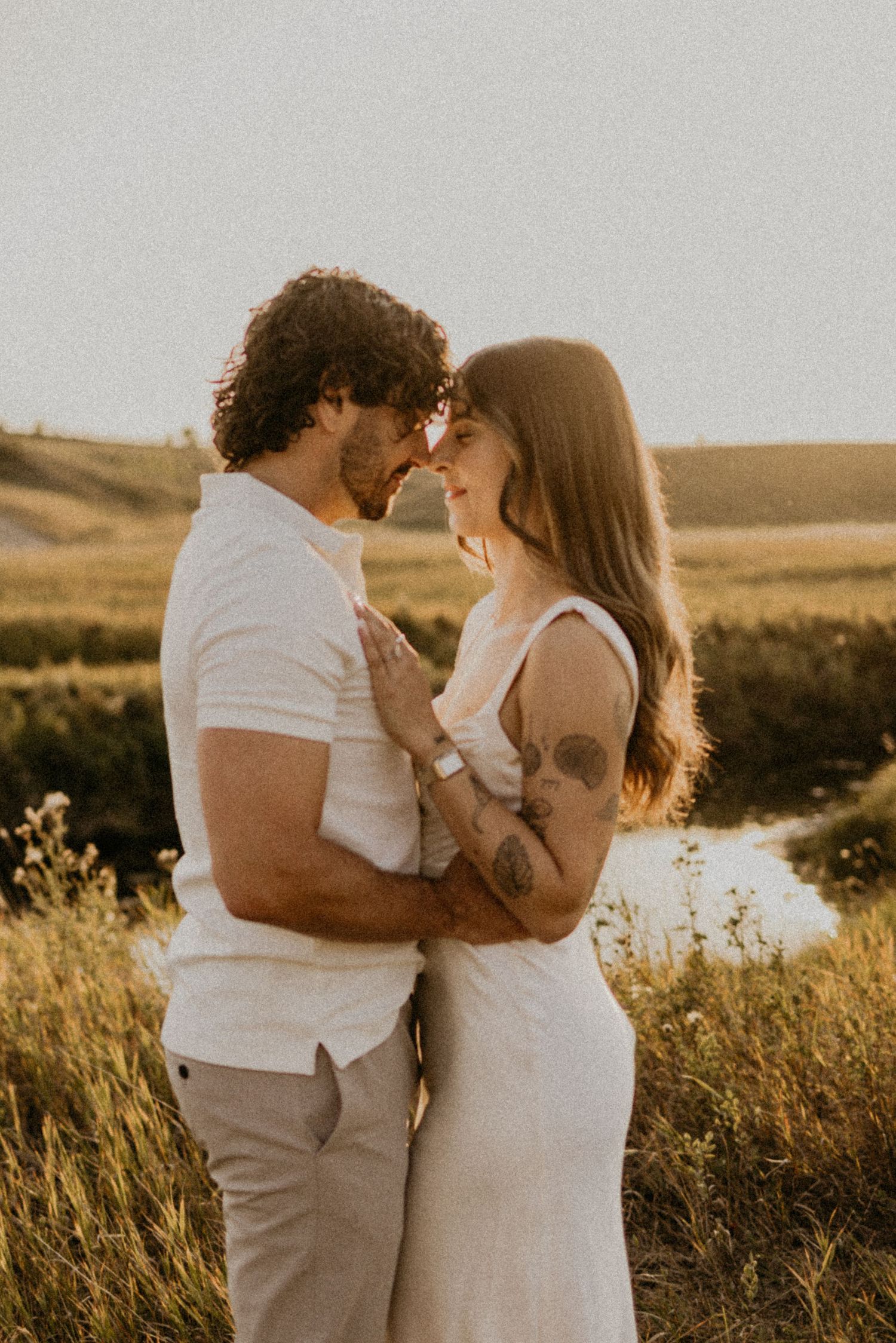 Couple embraces tenderly in a golden sunlit field during sunset creating a romantic summer atmosphere.