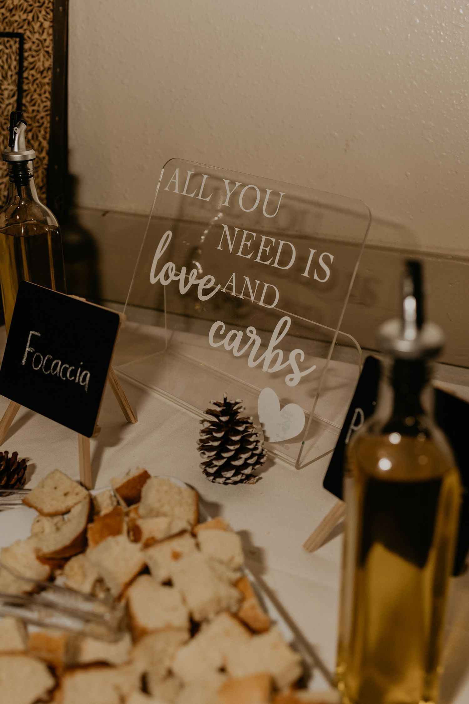 Decorative sign reading 'All you need is love and carbs' displayed near focaccia bread and wine.
