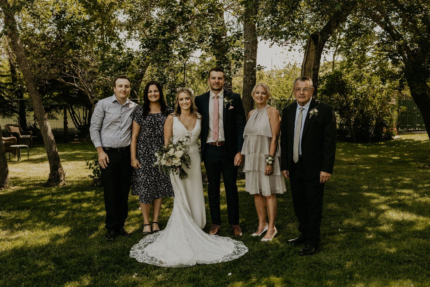 Small wedding group portrait taken outdoors with trees in the background.