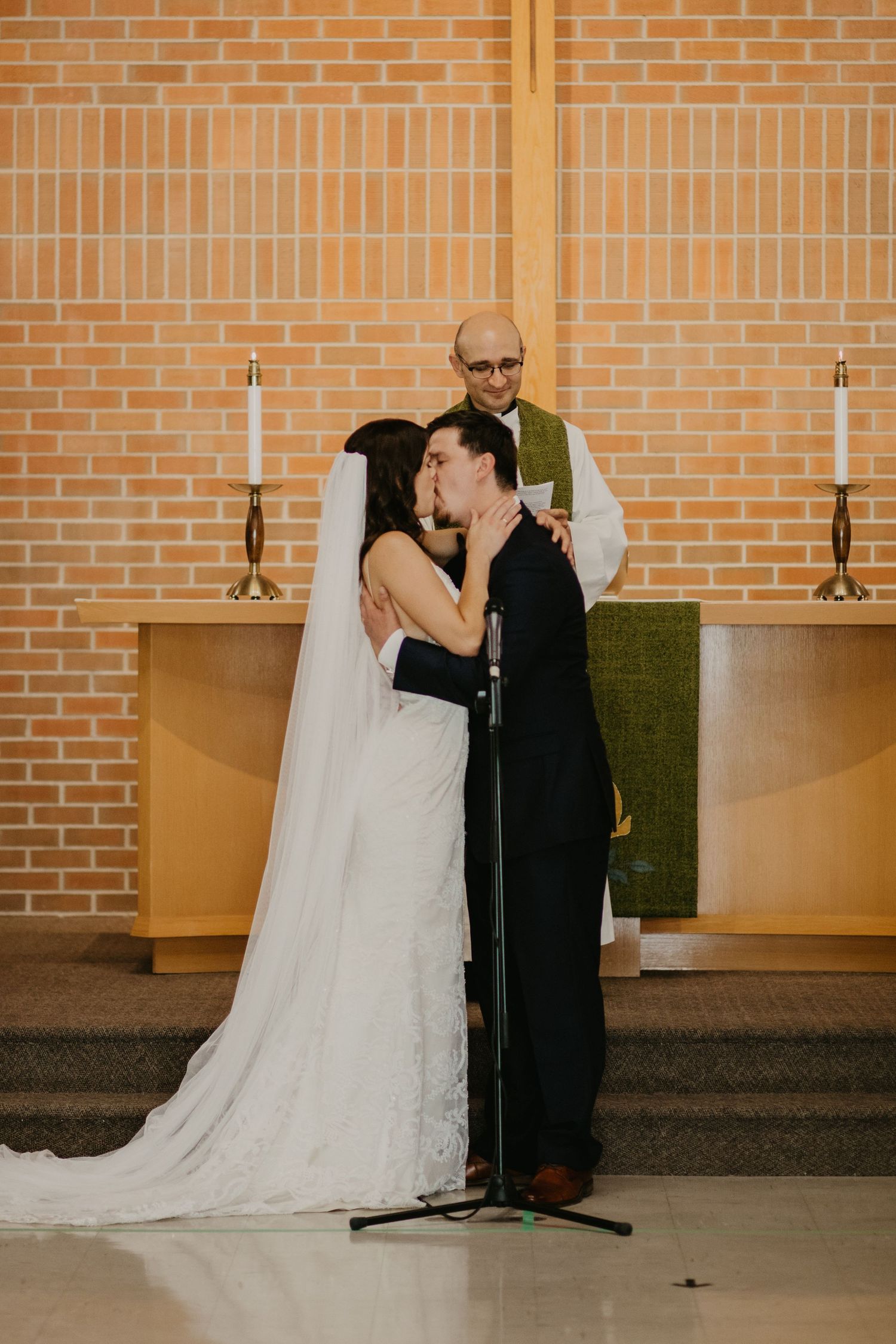 A tender moment during a wedding ceremony in a church with brick walls and candlesticks.
