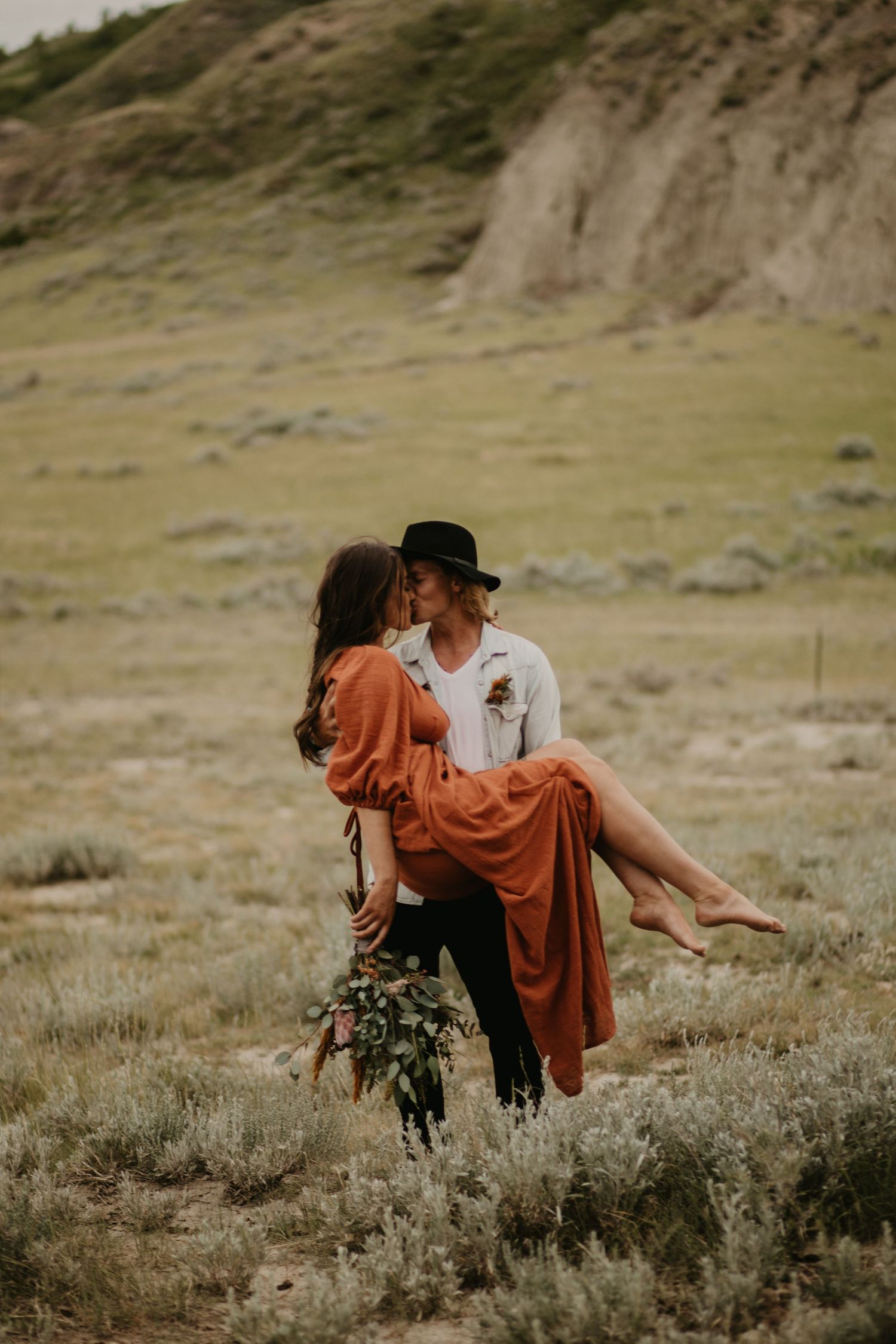 Intimate moment captured in a desert setting with flowing rust-colored dress.
