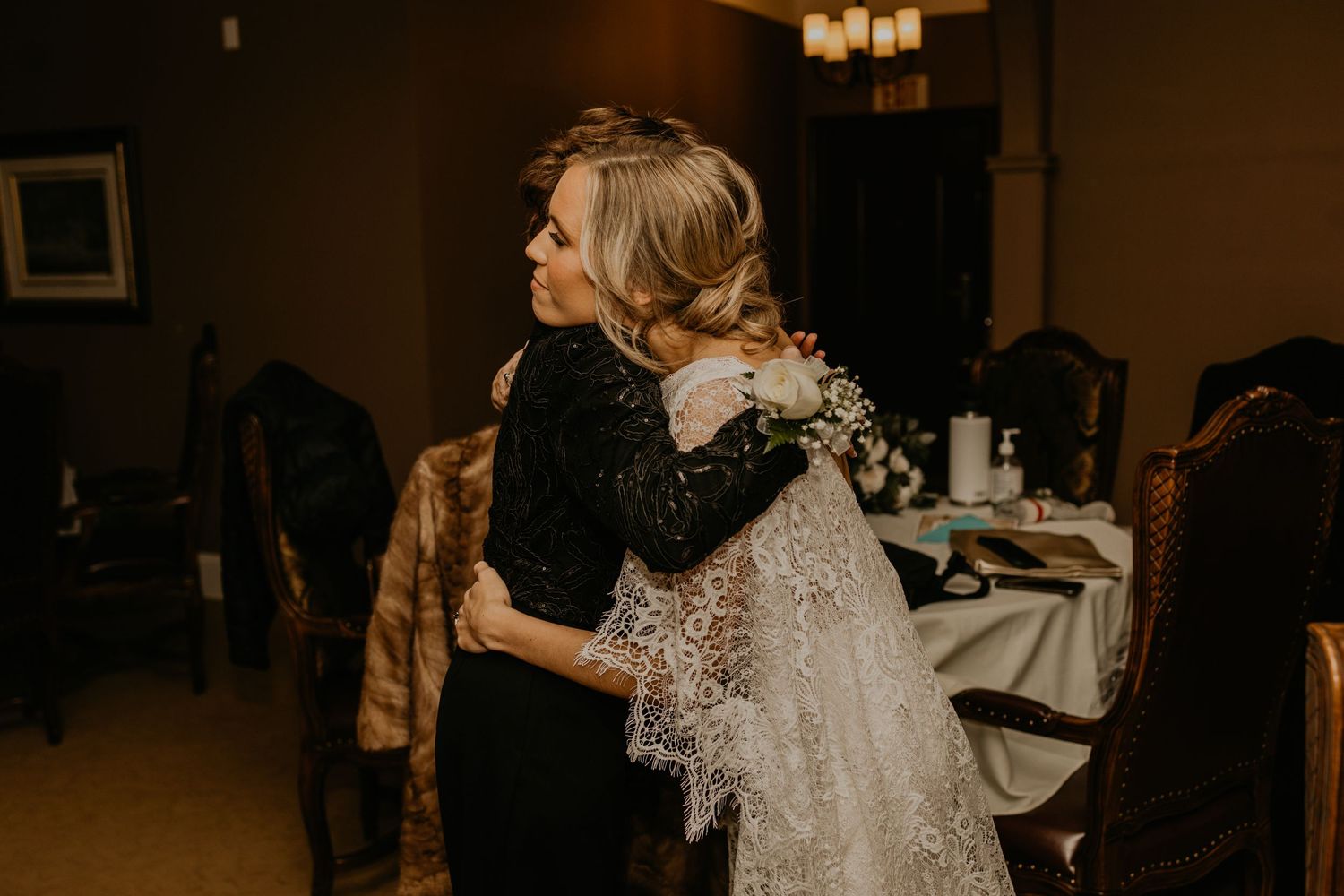 Two people share an emotional embrace at a wedding celebration in a dimly lit reception room.