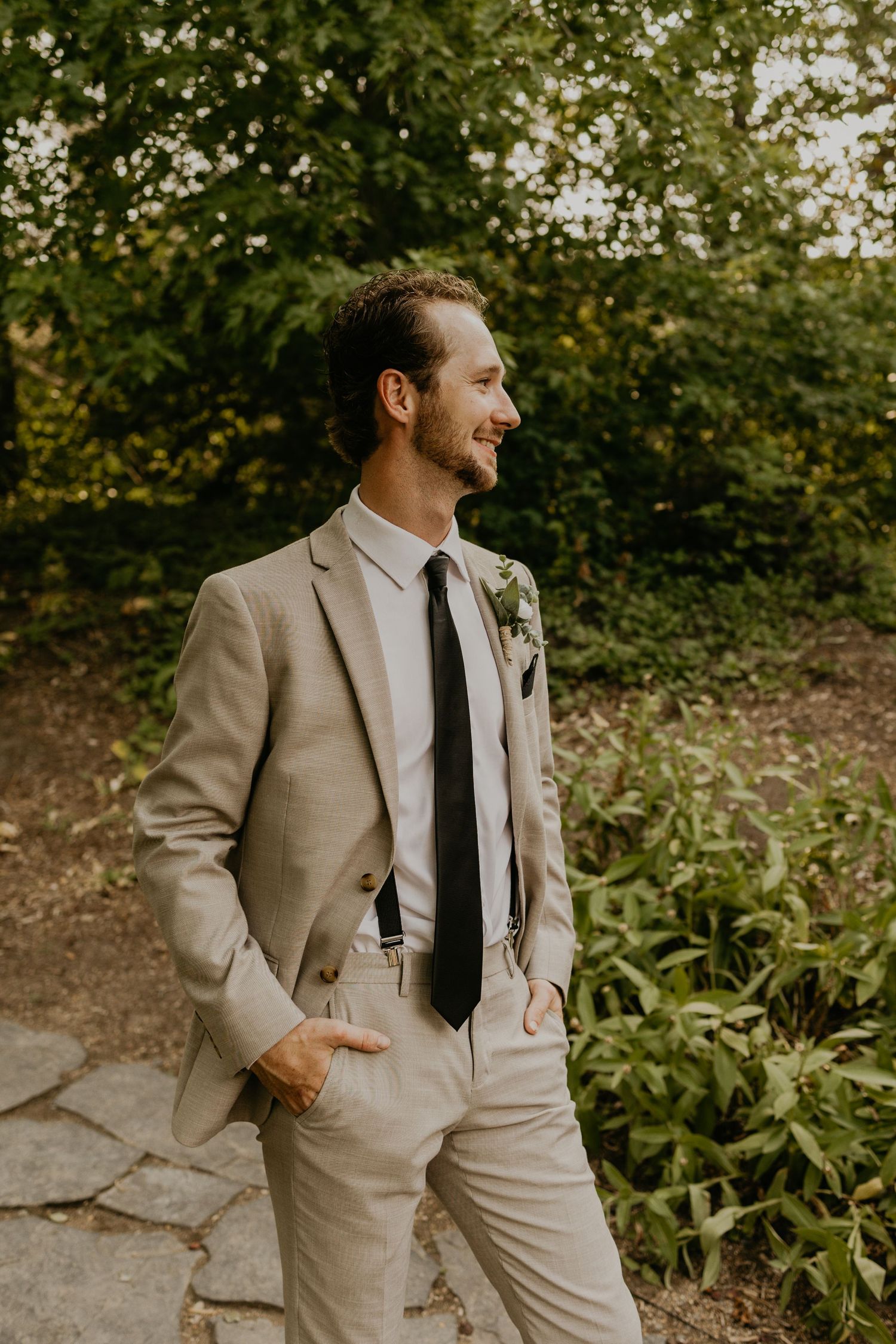 A person in a light beige suit smiling in a garden setting with natural greenery in the background.