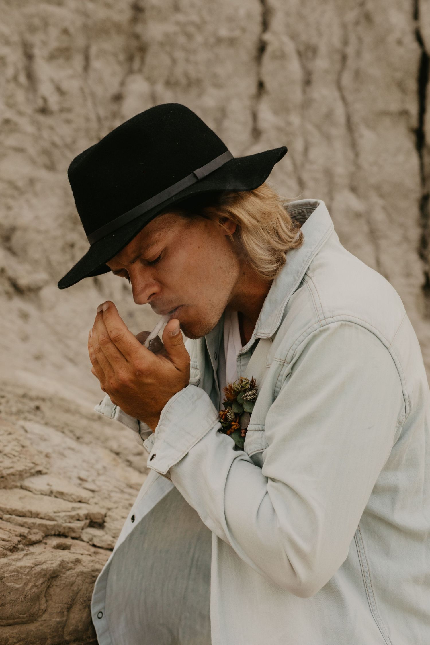Person in a white jacket and black hat holds a bouquet against a textured stone wall.