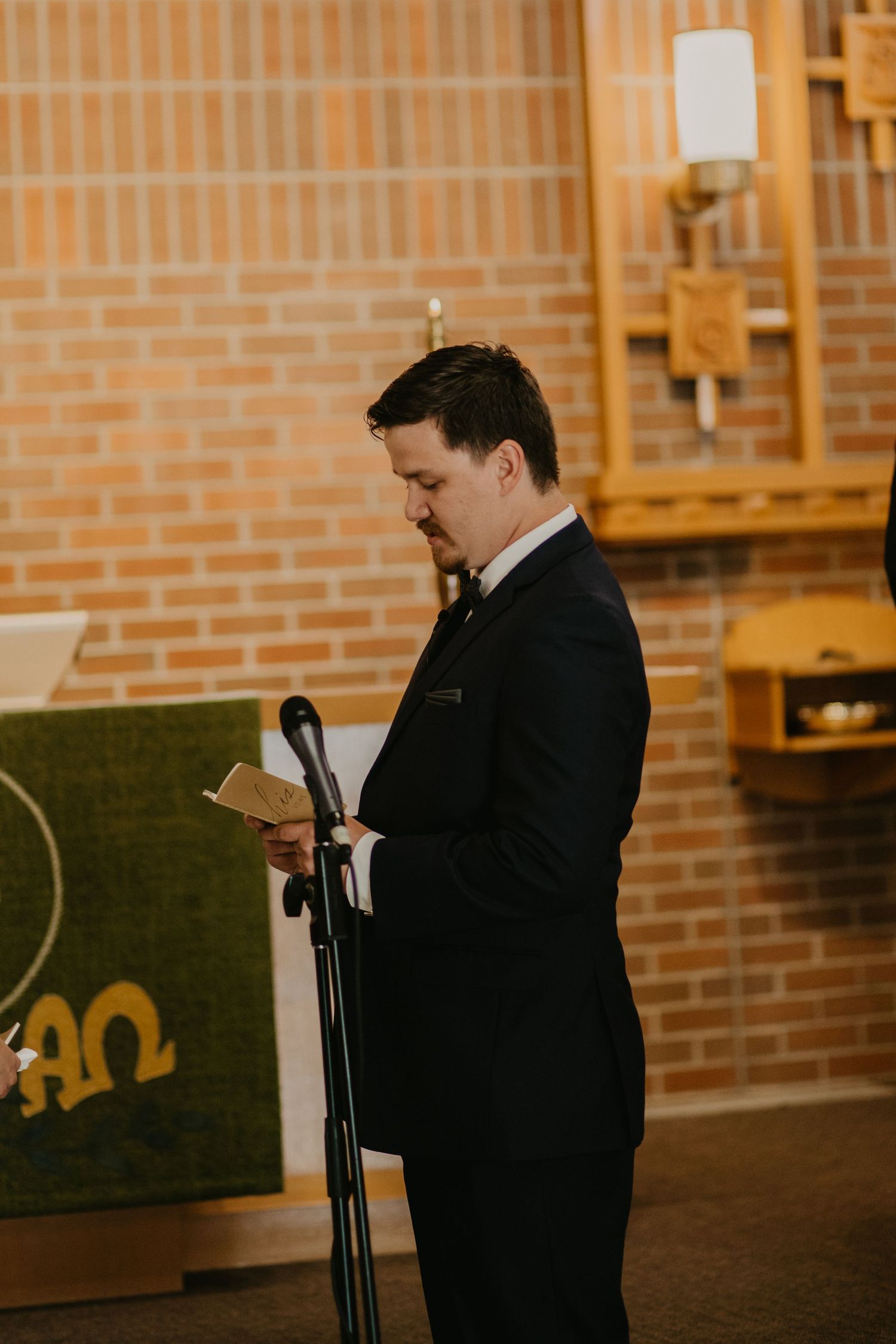 A person in formal attire reads from notes at a microphone during a ceremony.